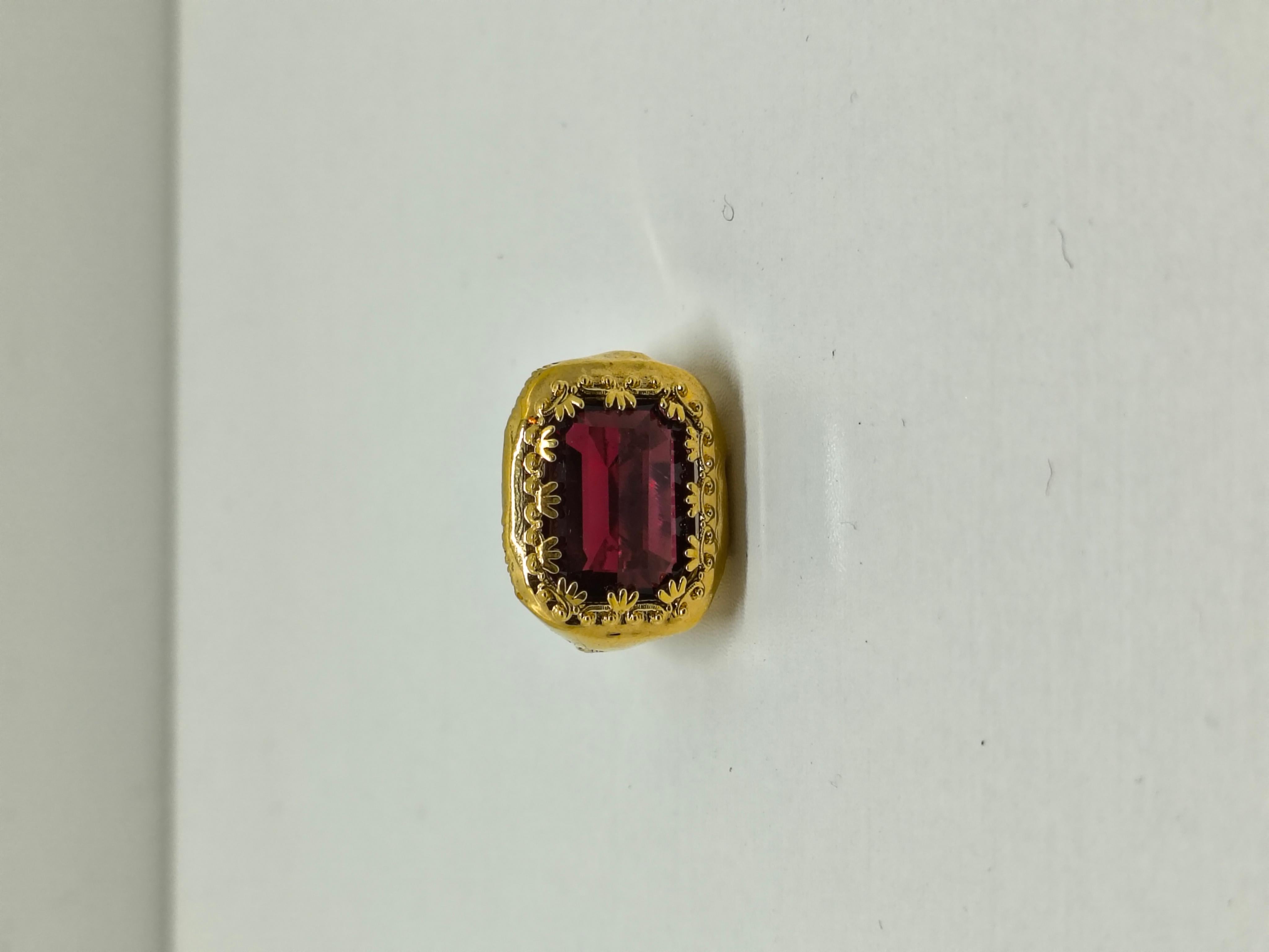 Der Bally Antique Gold Ring ist ein zeitloser Ausdruck von Vintage-Eleganz. Er präsentiert einen atemberaubenden roten Kristall im Smaragdschliff, der in ein kunstvoll gestaltetes, antikgoldfarbenes Band eingefasst ist. Der tiefrote Farbton des
