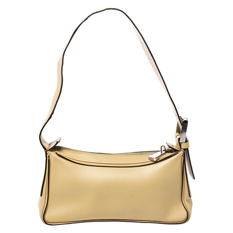 This lovely creation comes from the house of Bally. Crafted in Italy, it is made of quality leather and comes in a lovely shade of light yellow. This shoulder bag is held by a single handle with a buckle carrying the brand logo. It comes with a