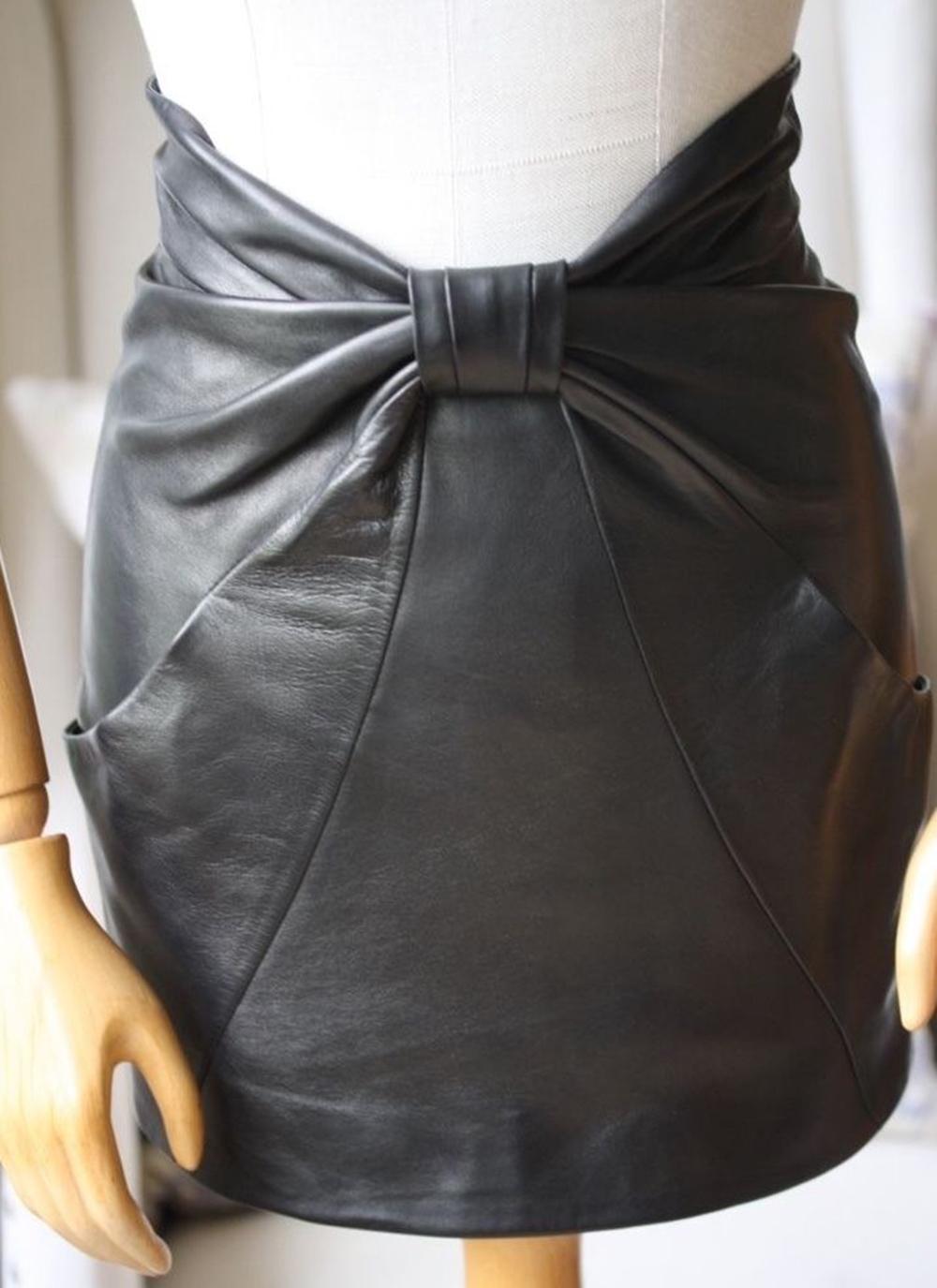Black lamb’s leather skirt with large leather bow at front from Balmain. Bow makes up both the front of the garment and the two hip pockets. Long gunmetal tone zipper at rear. Fully lined in black cotton-blend. Darts for shaping at front and rear.