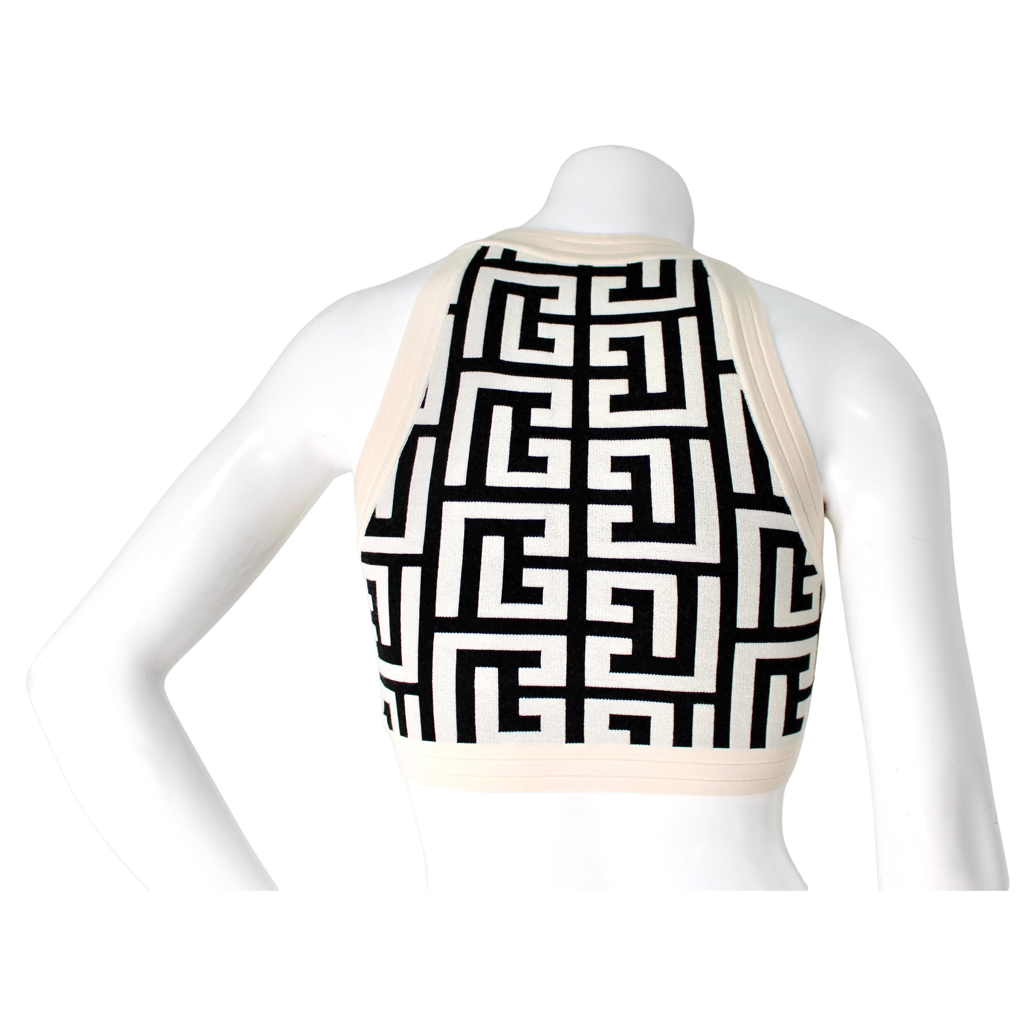 Le débardeur sans manches Monogram crème et noir de Balmain est une pièce saisissante qui incarne l'esthétique luxueuse et avant-gardiste de la marque. Ce haut présente une base crème élégante ornée du monogramme noir emblématique de Balmain, créant