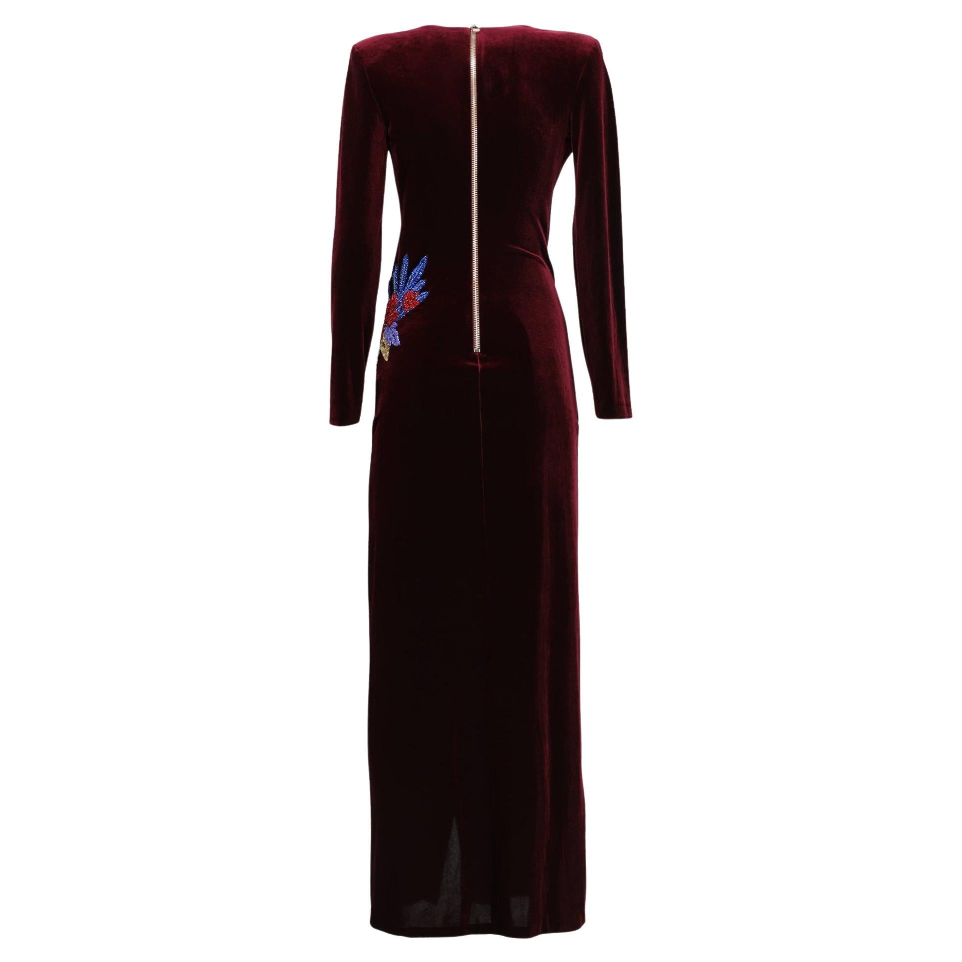 Balmain velvet wrap gown in burgundy.
Polyester (92%) and elastane (8%). 
With shoulder pads, long sleeves, beads embroidery on the side of the waist, and high slit in the front side. Closes with gold-tone button on the back.

Total length 149