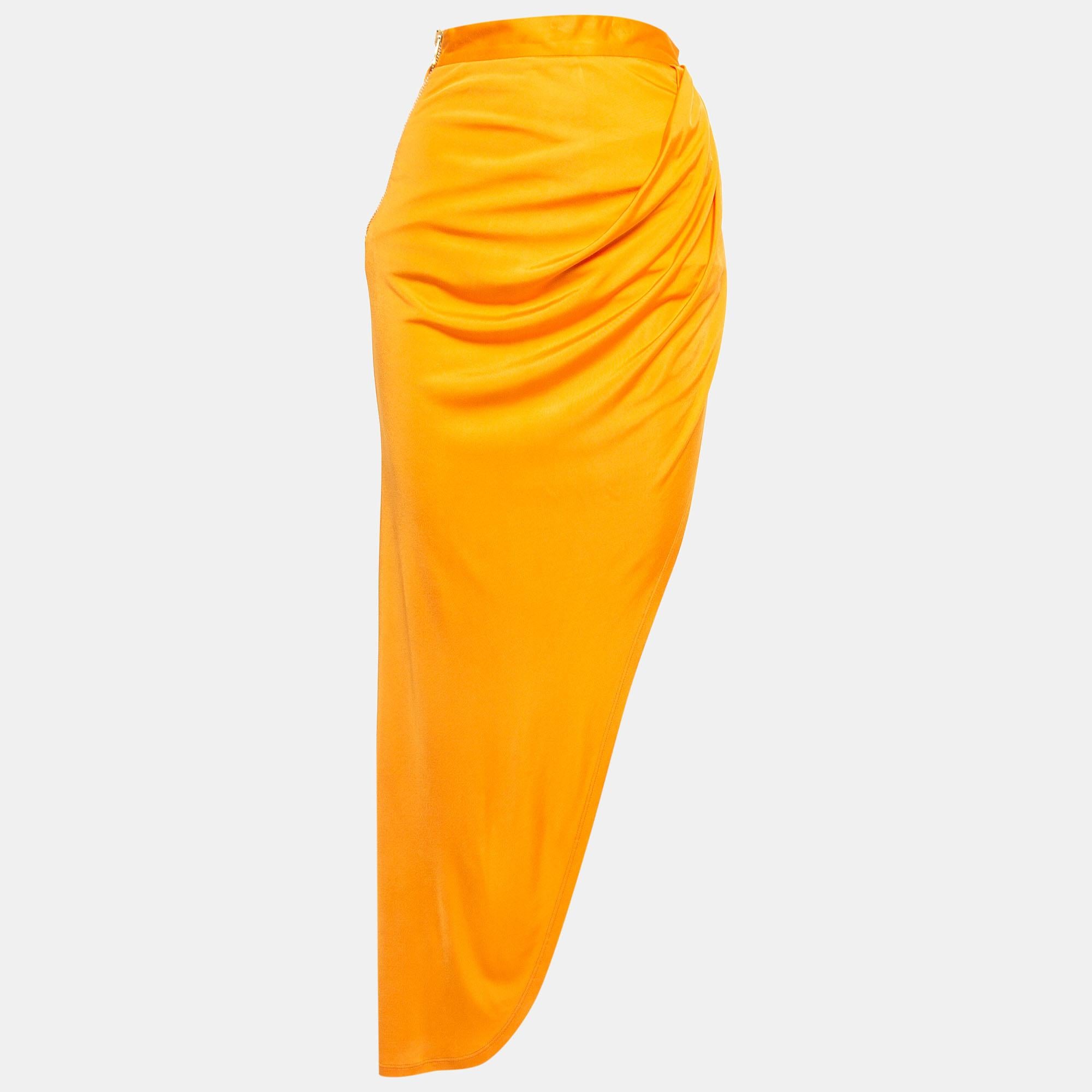 Tailored by Balmain, this vibrant orange jersey high slit draped maxi skirt exudes elegance and allure. Its flowing silhouette, adorned with a high slit, accentuates movement and grace. Perfect for making a statement, this piece effortlessly