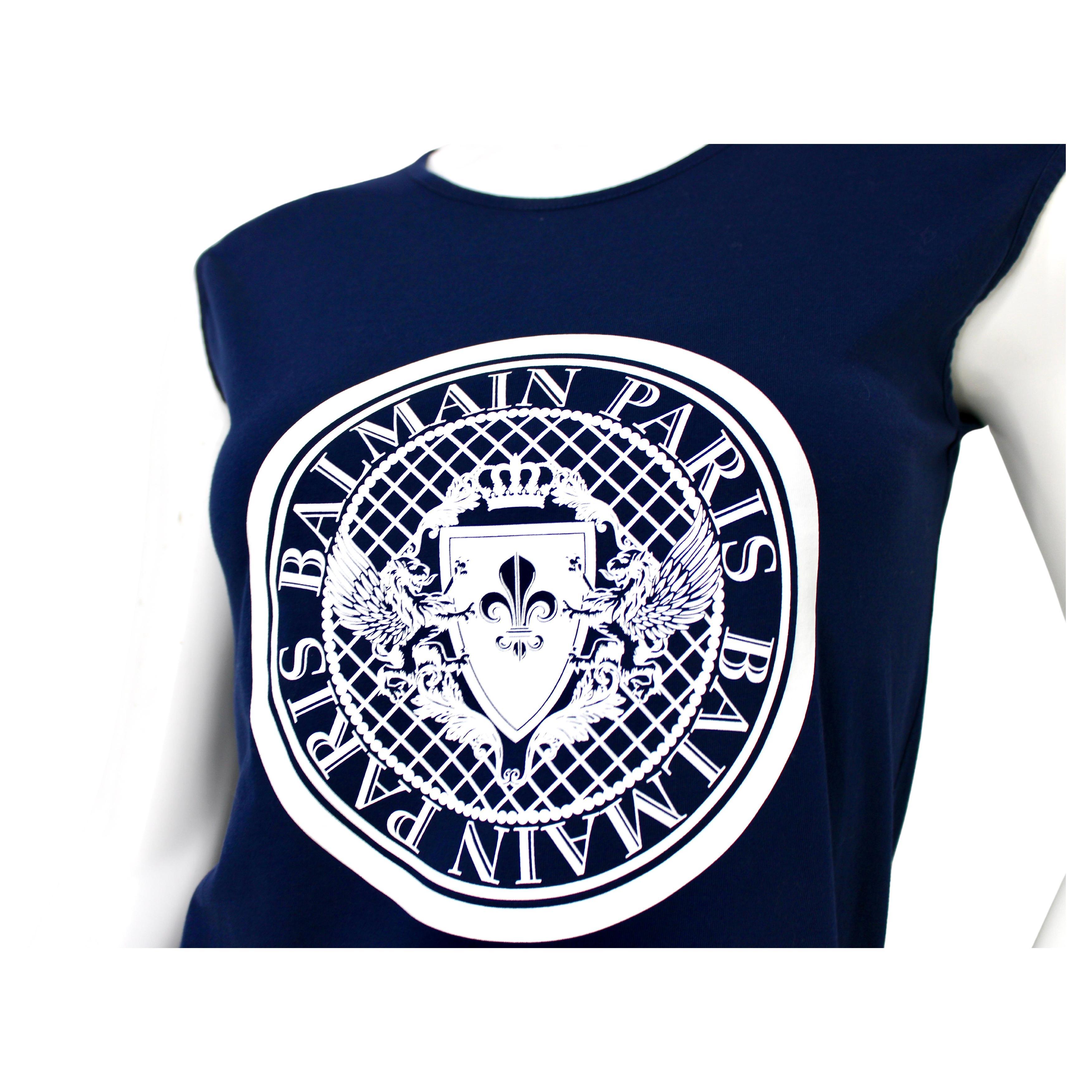 Le t-shirt à logo et médaillons aux épaules bleu marine de Balmain Paris est une pièce à la fois étonnante et décontractée qui incarne l'esthétique de luxe caractéristique de la marque. Confectionné en coton bleu marine de haute qualité, ce t-shirt