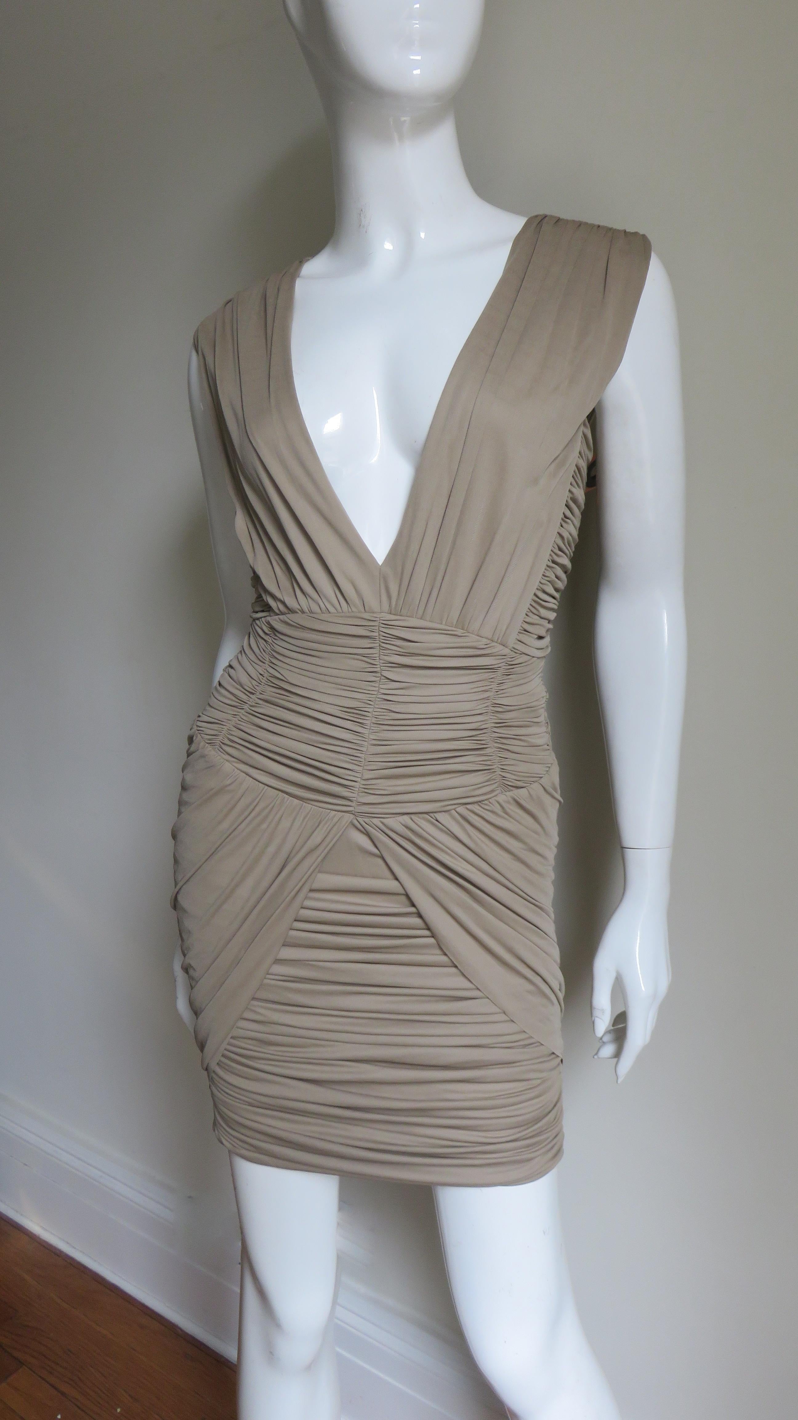 Un fabuloso vestido de jersey de seda fina color topo de Balmain.  Tiene un escote pronunciado enmarcado con paneles fruncidos verticales.  La falda entallada está fruncida horizontalmente con  inserciones en ángulo a ambos lados. La espalda del