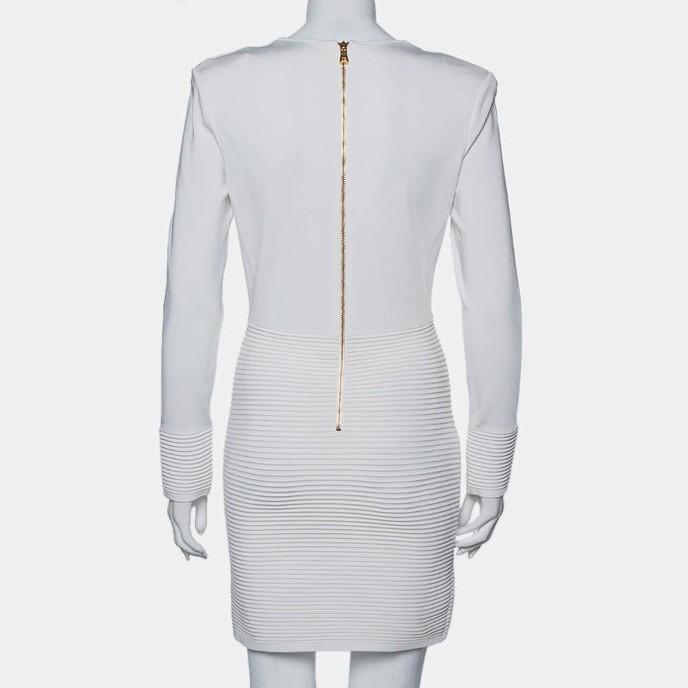 Highlighted by a plunging neckline with tie-up detailing, this Balmain white mini dress is a statement dress. The dress has a back zip closure and ribbed accents on the long sleeves and skirt. Style it up with eye-catching accessories.