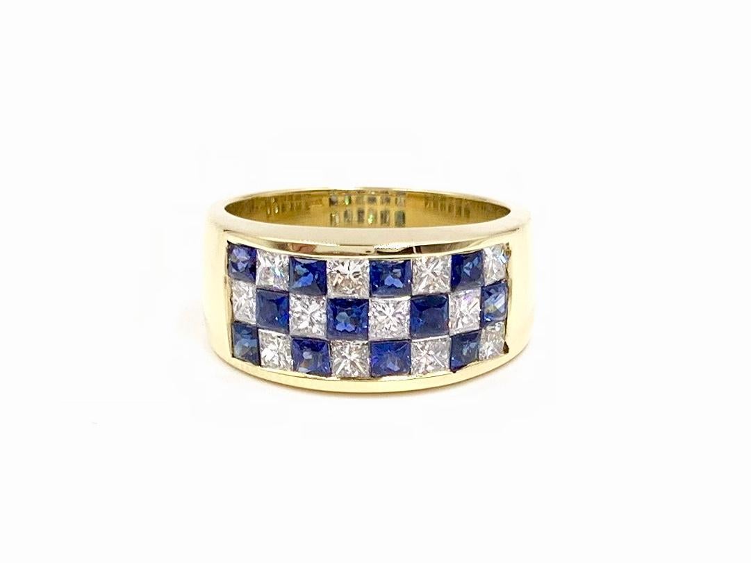 A beautiful 18 karat yellow gold 9mm band style ring featuring expertly invisibly set princess cut white diamonds and blue sapphires in a checkerboard arrangement, finely crafted by Balogh. Ring consists of 1.21 carats of vibrant, well saturated