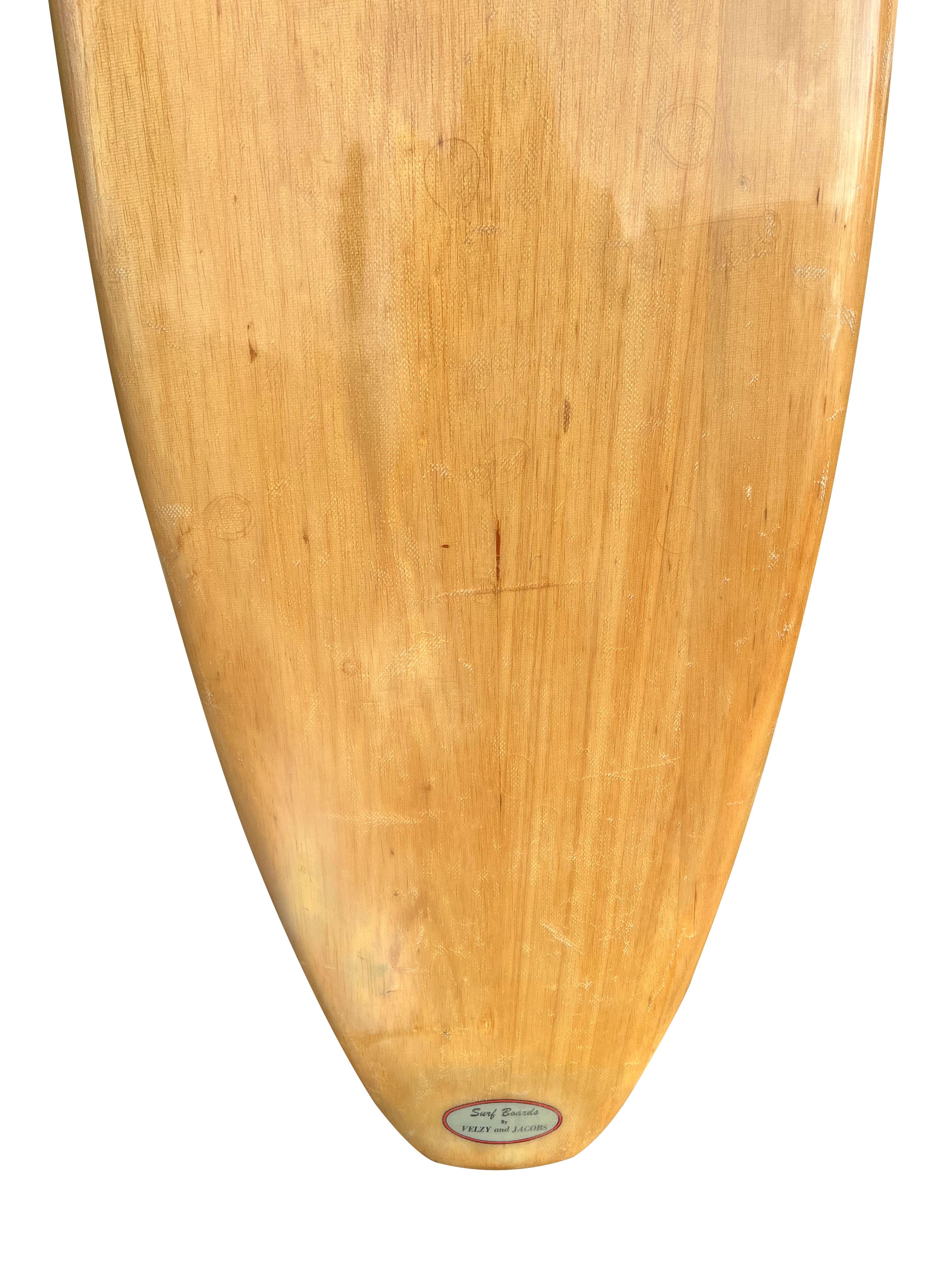 A classic piece of surfing history, this balsawood longboard created by famed Hap Jacobs has the distinctive pig shape design with original early redwood fin. 8’7 rounded tail. Featuring the “Surfboards by Velzy and Jacobs” logo used for a brief
