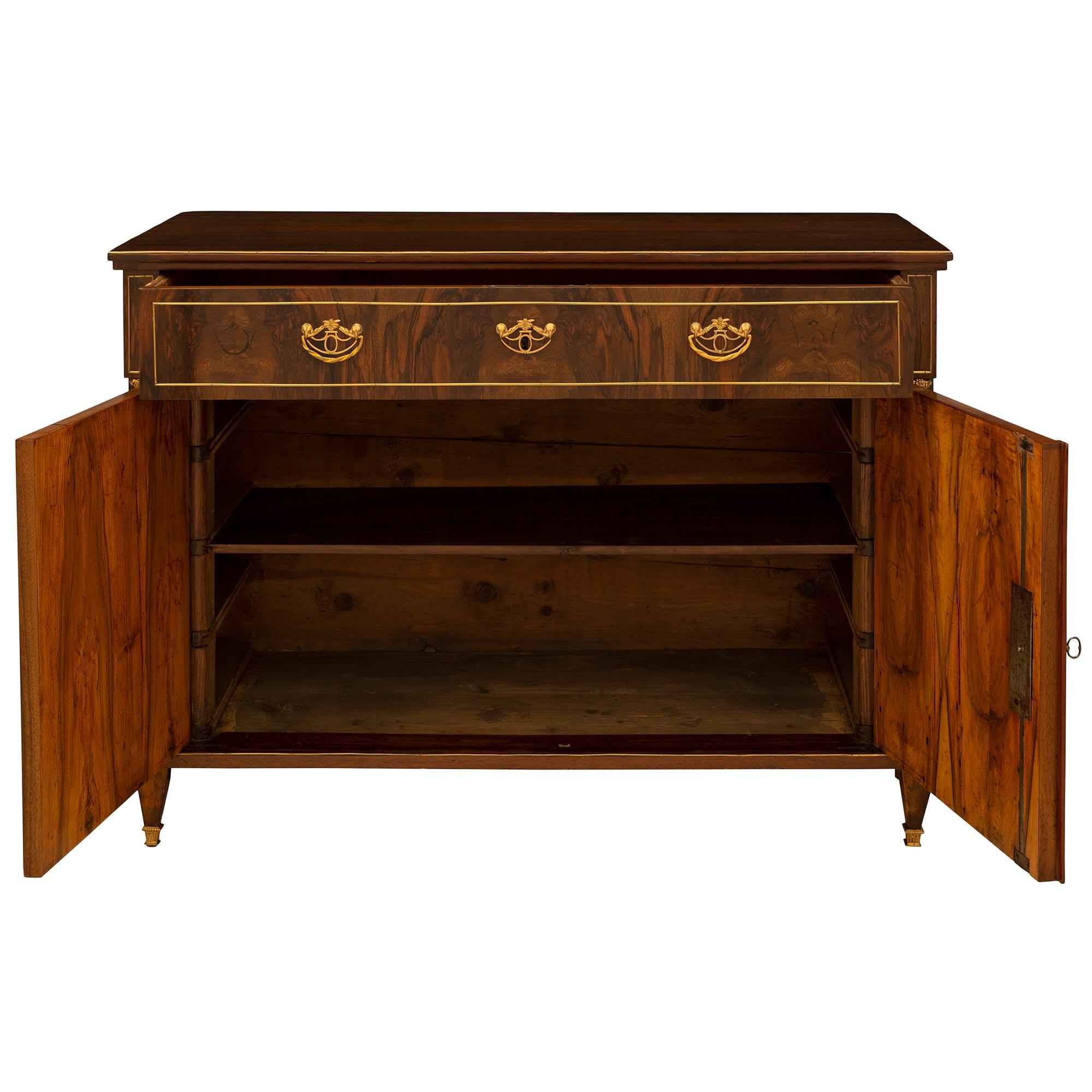 A very handsome Baltic-Continental mid-19th century neoclassical style walnut commode. The two-door and one-drawer commode is raised by square tapered legs ending with square ormolu sabots. The straight frieze is below two doors with ormolu keyhole