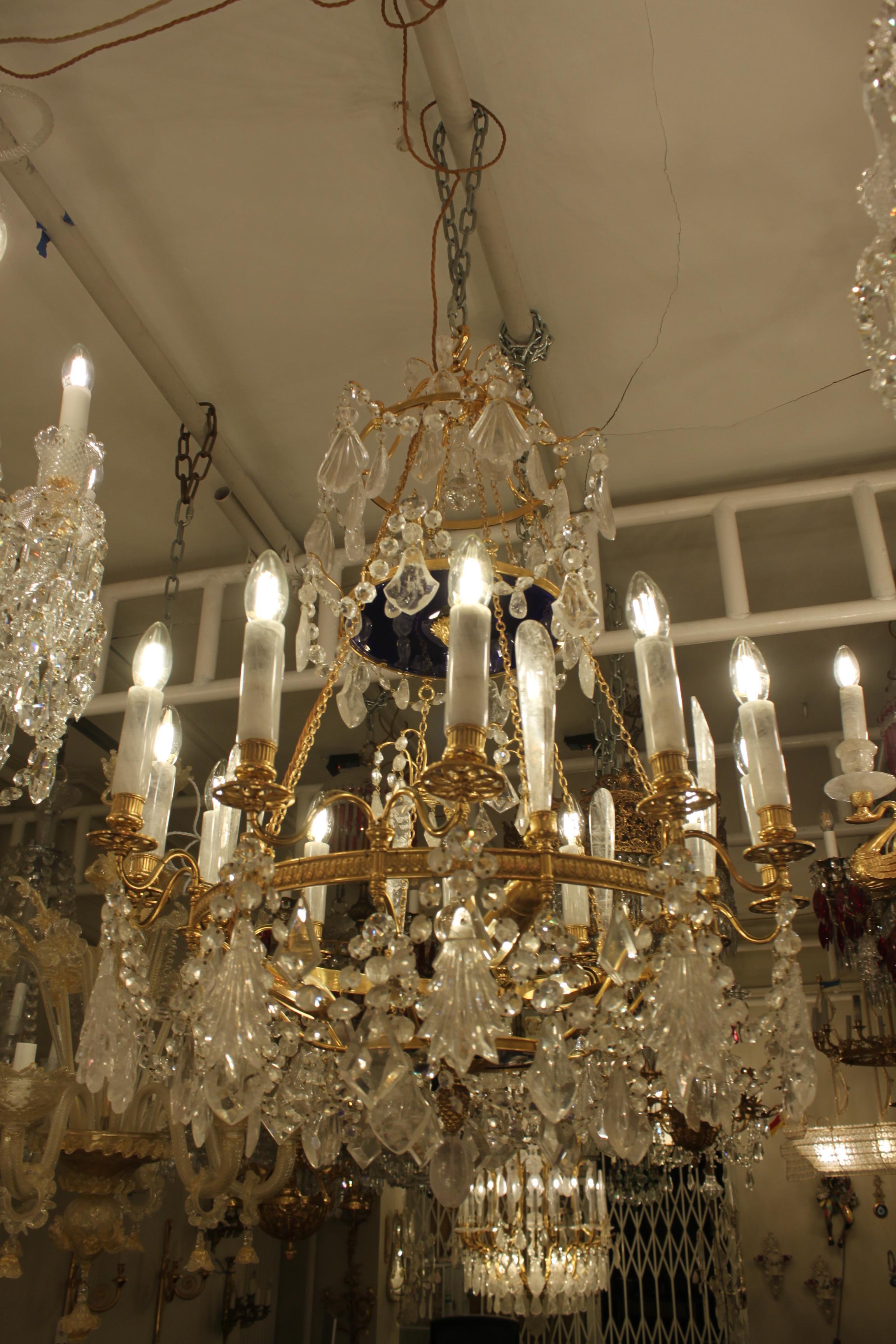 A beautiful 15 light 4 tier chandelier in bronze and rock crystal. 
An outer ring of 12 gilt drip pans a-topped with rock crystal candle tubes and 12 x E14 candle bulbs below which hang alternating fern and clam shell rock crystal drops connected to