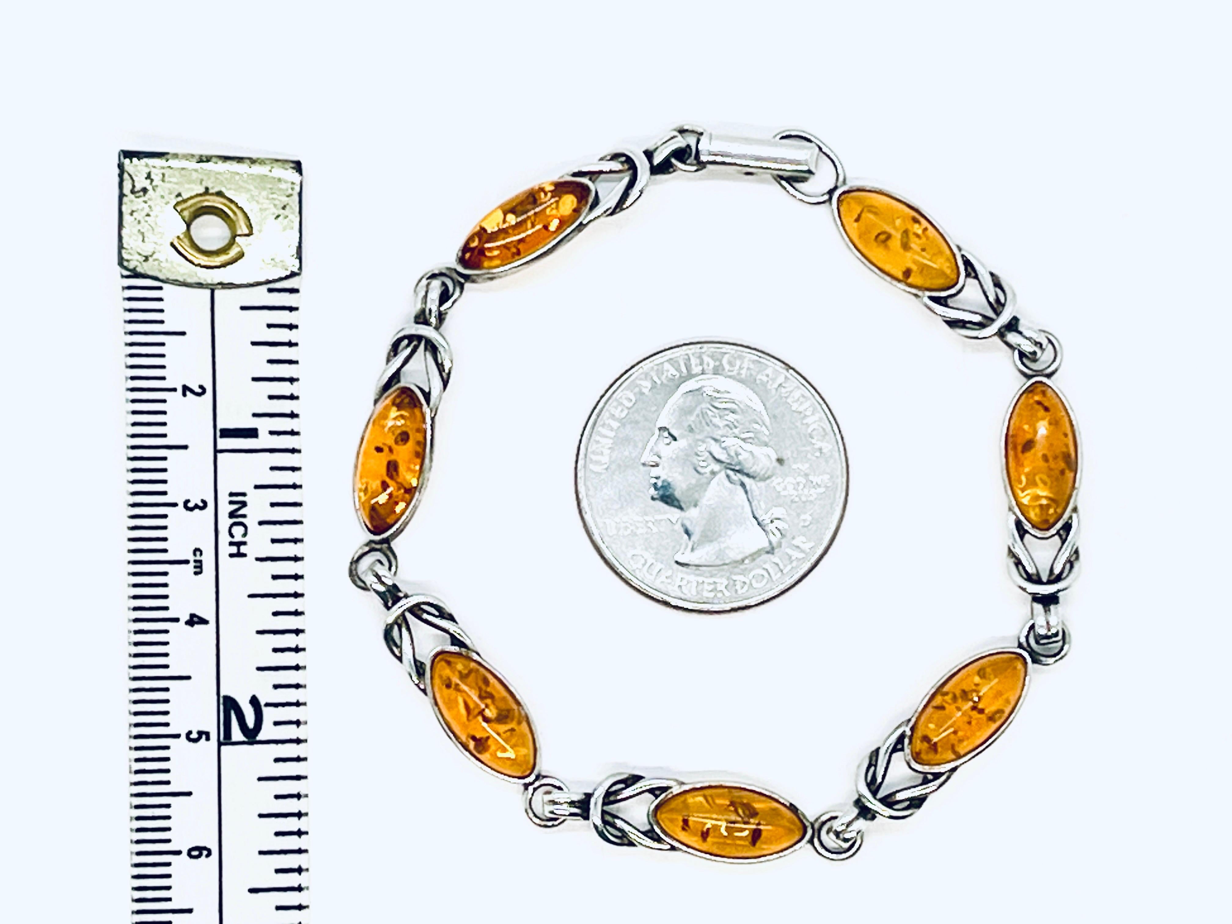 7 cabochons marqués d'ambre baltique sur un bracelet à maillons en argent (marqué), avec des détails de faux nœuds. Fermoir à charnière. Deux marques : Une seule visible à la loupe sur l'argent sous l'un des cabochons d'ambre près du fermoir. La