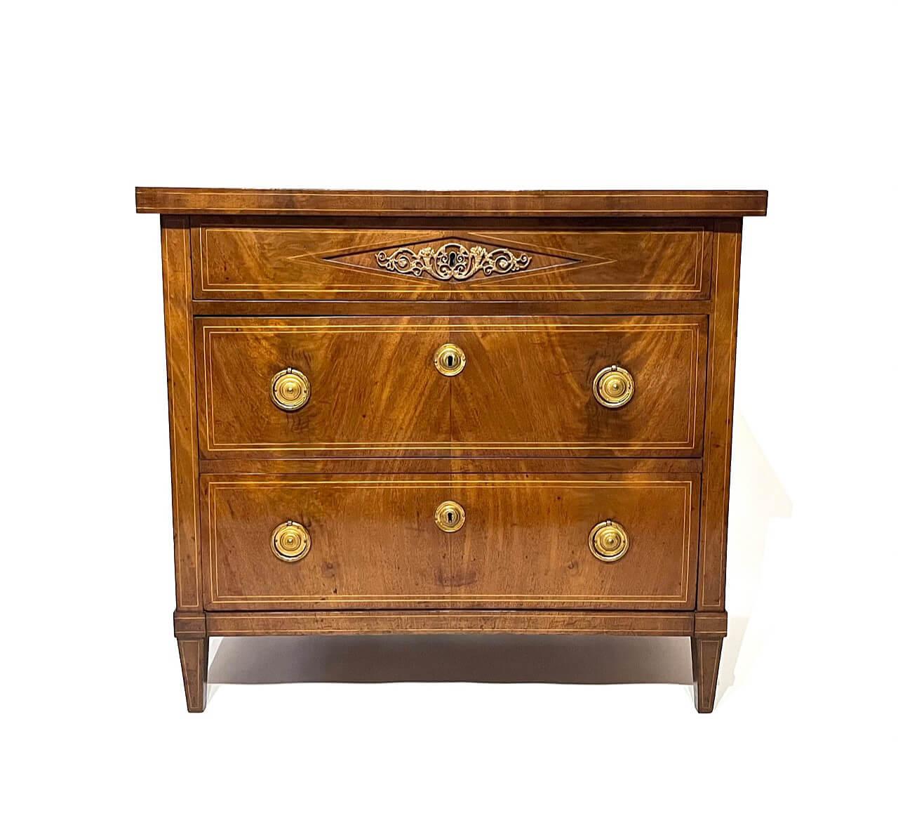 An elegant circa 1800 Prussian Baltic Directoire style three drawer commode having luminescent mahogany veneered and satinwood line-inlaid oak and pine case, the thick slab top above locking top drawer with center cornucopia and foliate scroll