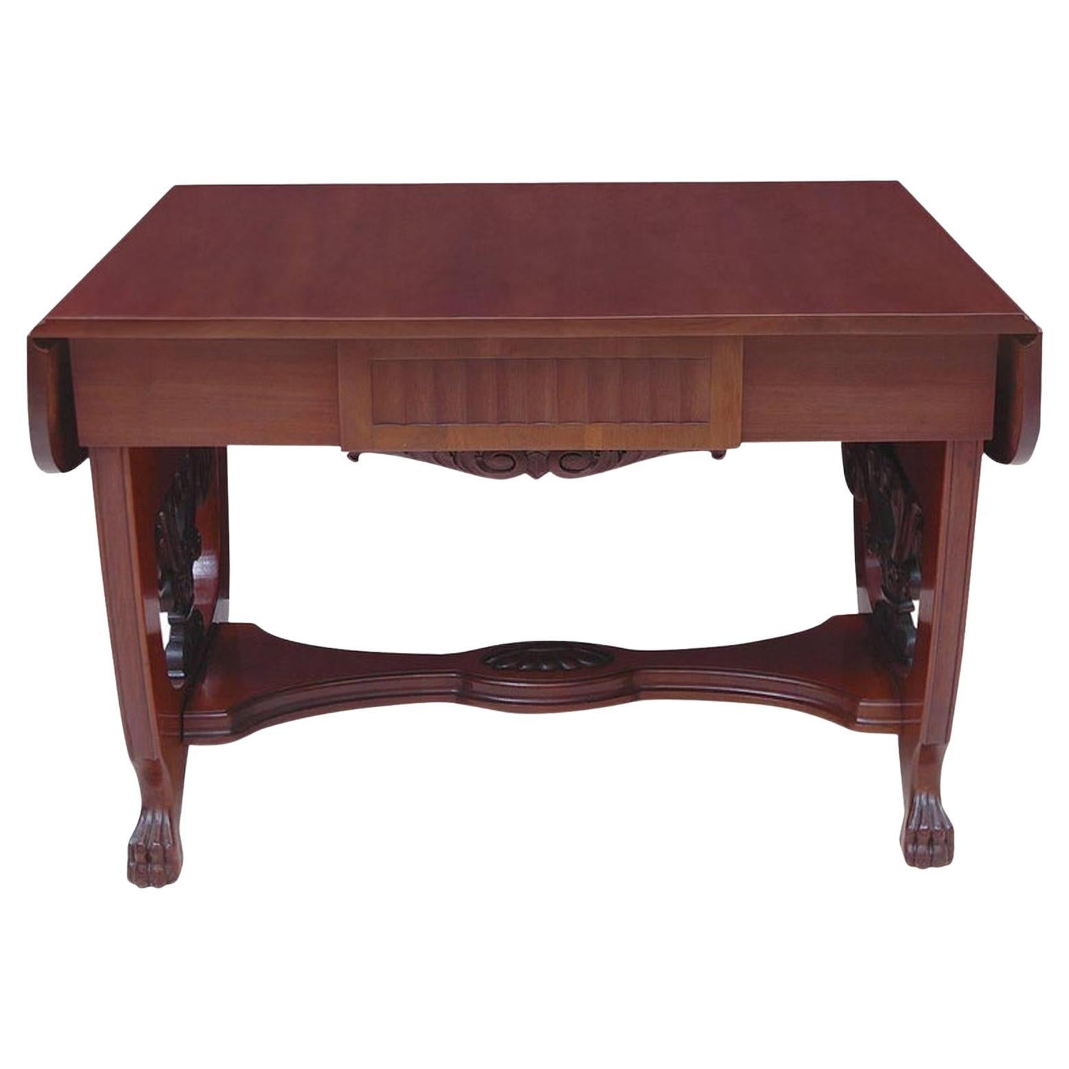 A very fine Baltic writing or sofa table in the Empire style (and edging toward the Art Deco period that would follow.) In Cuban mahogany with carved trestle-base ending in carved lion's paw feet. Features two drop-leaves and one-drawer. French