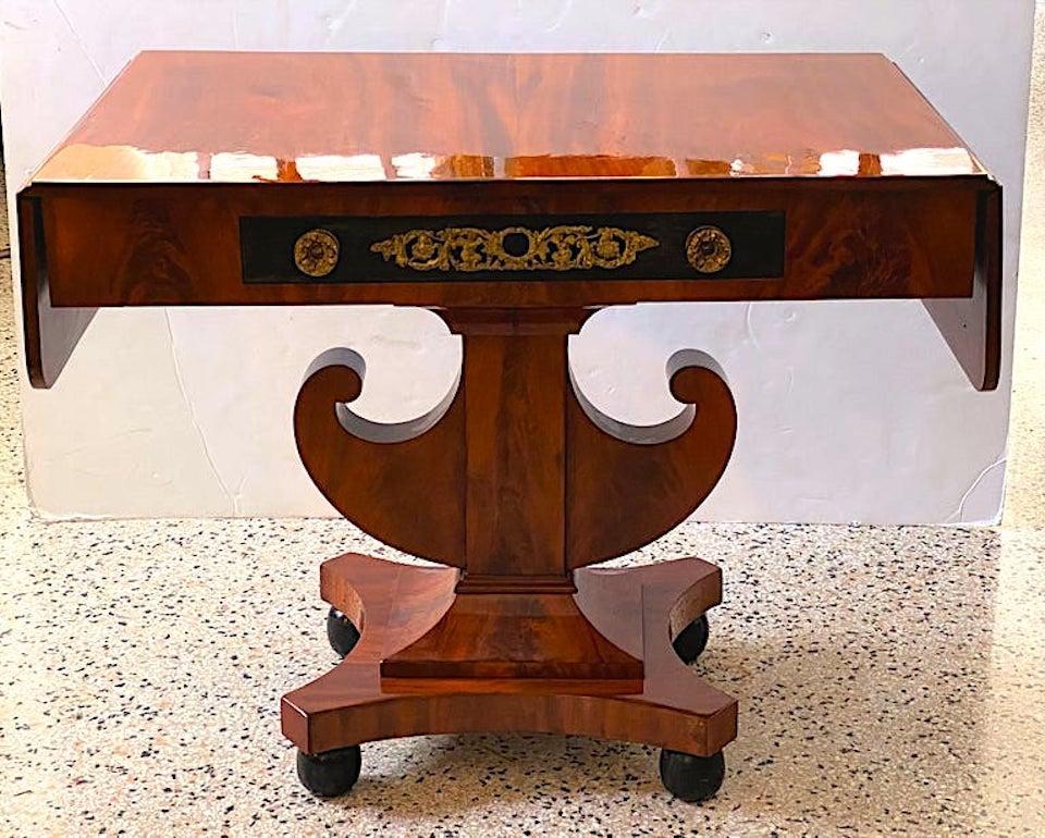 This stylish English Regency inspired mahogany Baltic library table dates to the 1820s-1830s and was acquired from a Palm Beach estate. The piece has a beautiful French polish, gilt bronze mounts, and ebonized black panel. There is a single drawer