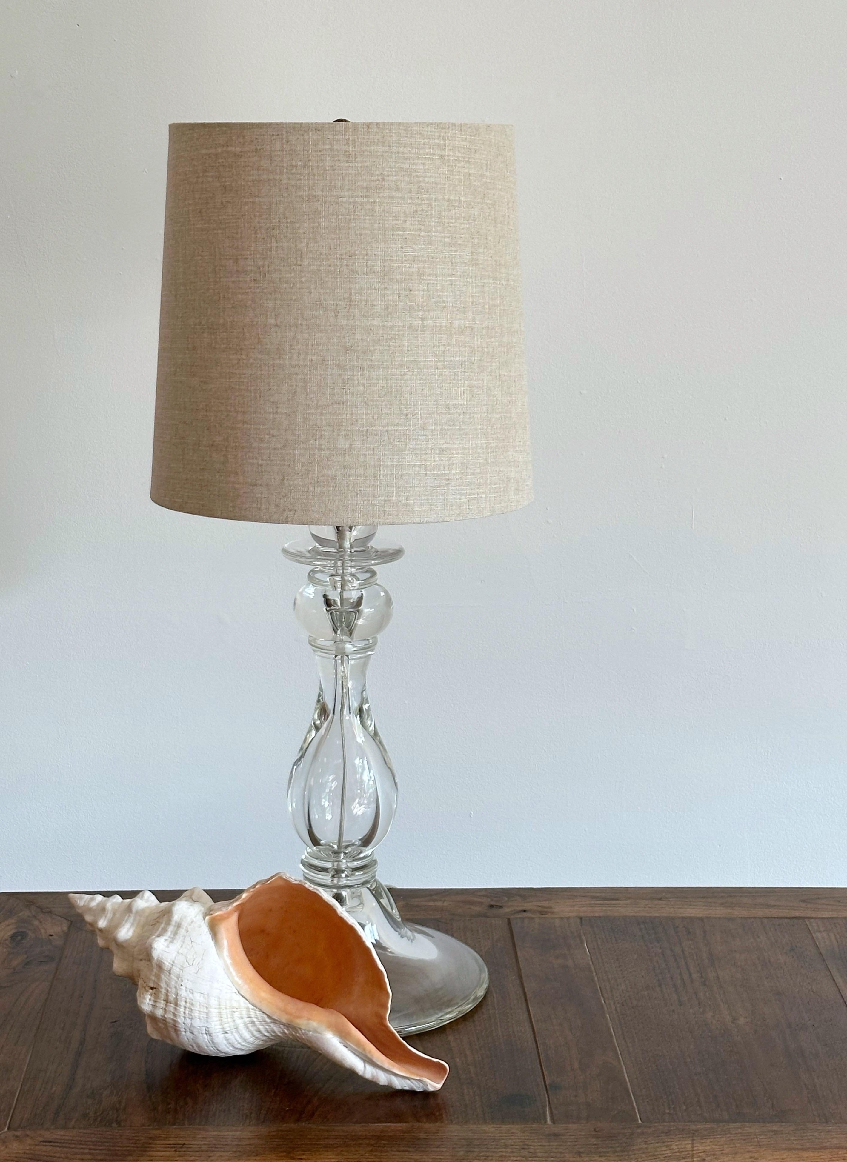 A large clear glass table lamp. Baluster style silhouette. Double light fixture with patinaed brass hardware. Shade not included.