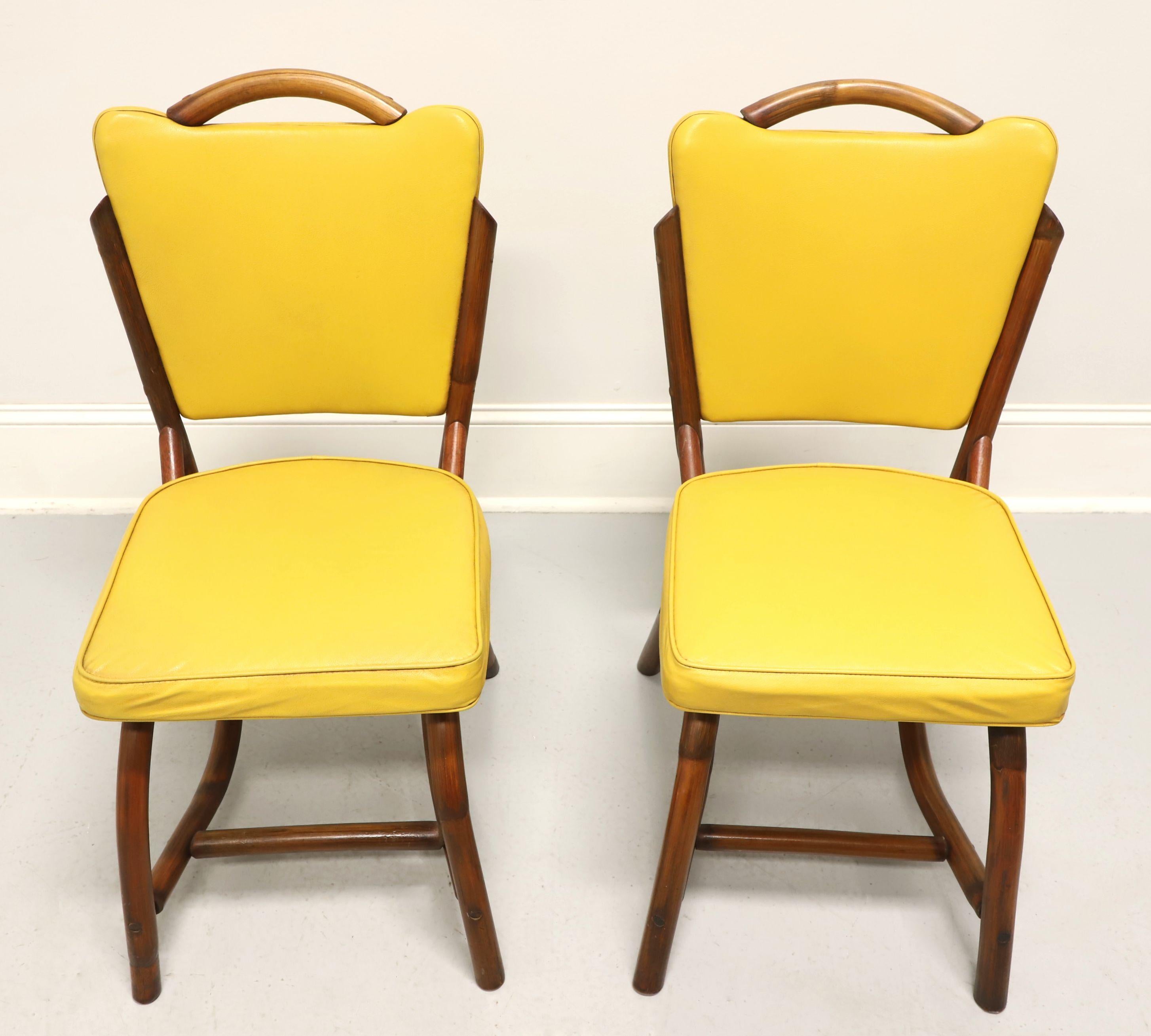 A pair of mid 20th century Coastal style dining side chairs by Bam-Tan Products. Rattan with a distinctive mid century modern style, rounded back with flared corner yellow colored vinyl upholstered backrest, arched legs and stretchers supporting