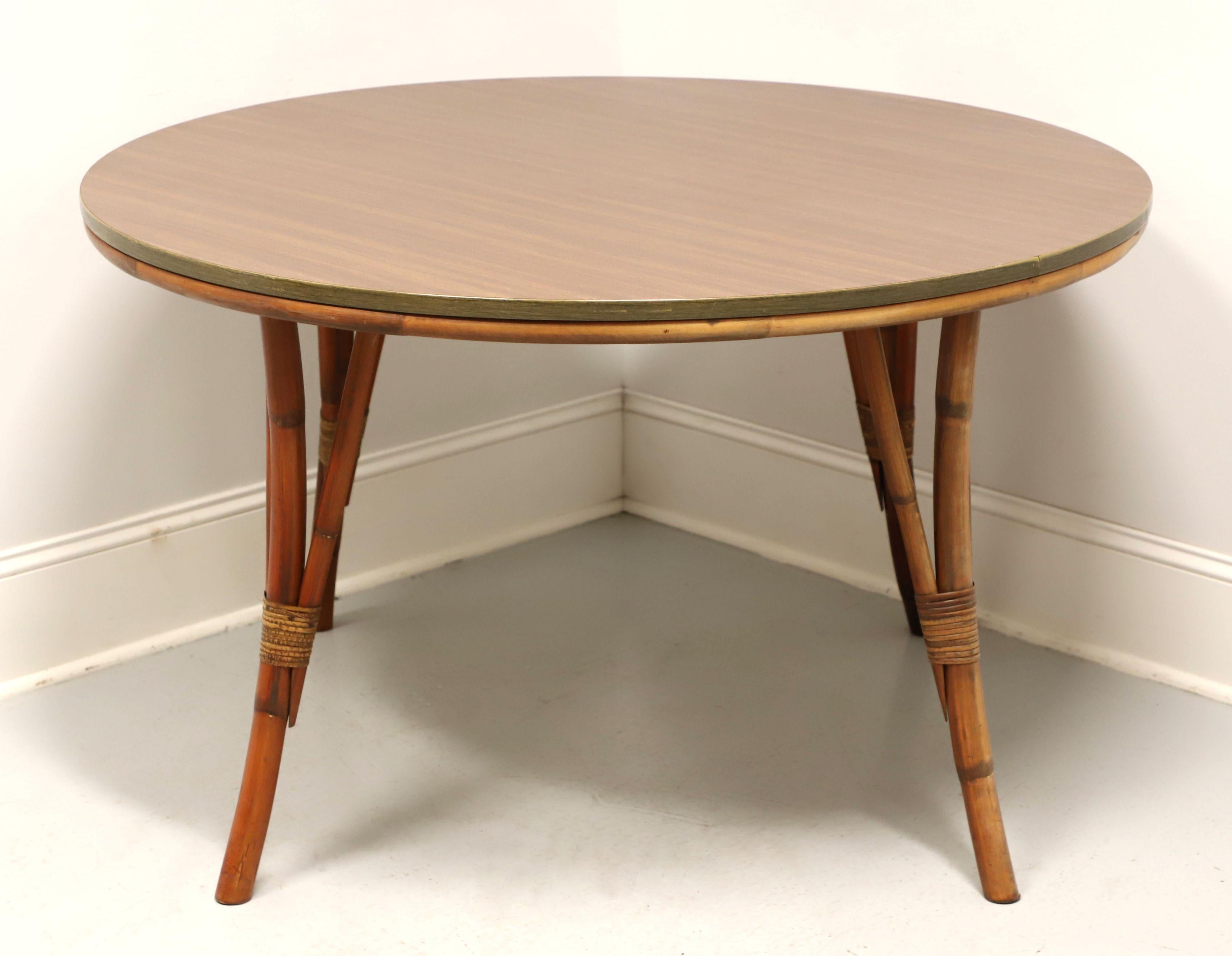 A mid 20th century Coastal style dining table by Bam-Tan Products. Rattan with a distinctive mid century modern style, laminate wood grain top, wood grain metal edge, rattan apron, and flared three-prong round legs with decorative rattan strapping.