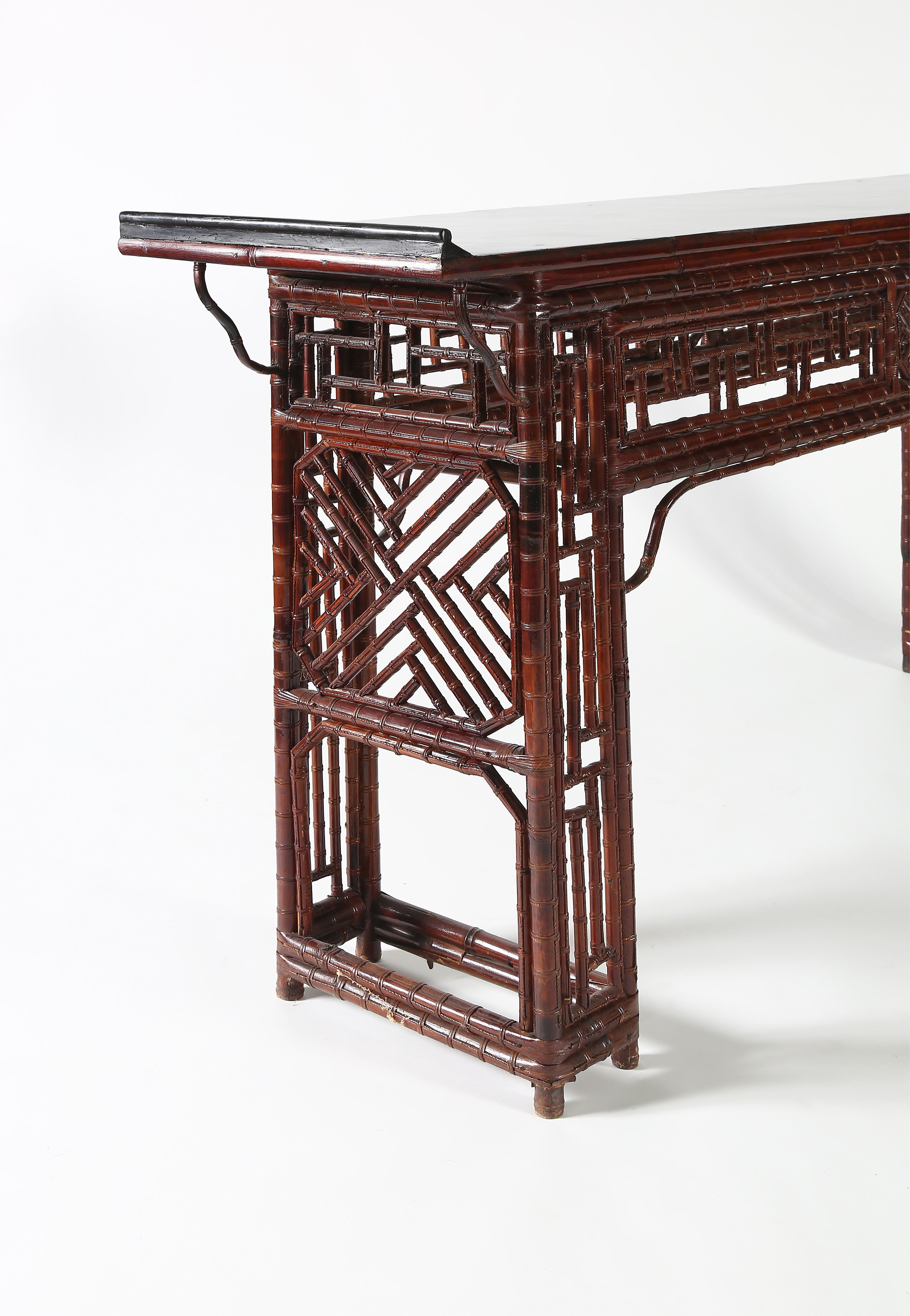 The table with a black lacquer flank top ending in everted flanges, above wrapped around stretchers, fretwork paneled apron with attached shaped spandrels, supported on recessed legs consisting of posts enclosing open lattice panels and braced with