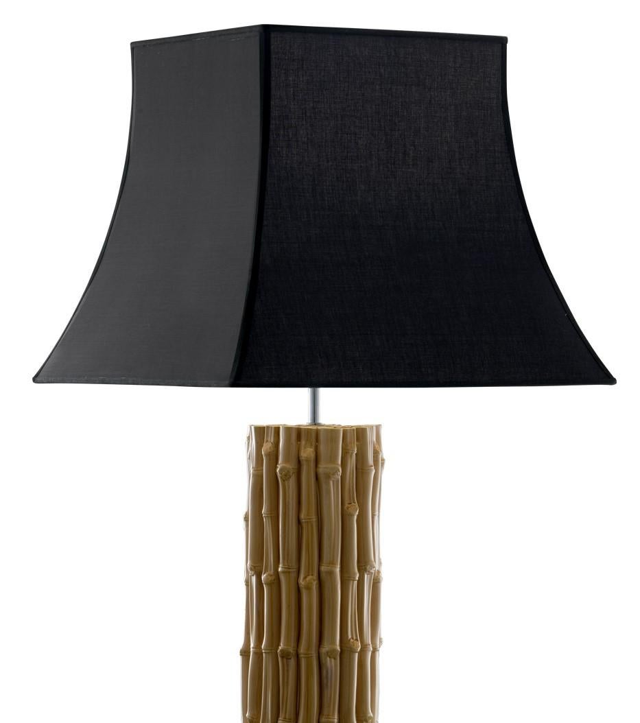 The ceramic body of this lamp reproduces in all its details a vertical structure of bamboo sticks with a delicate amber color that makes the decoration even more life-like. The shade on top, in black with tonal accents on the edges, is shaped like