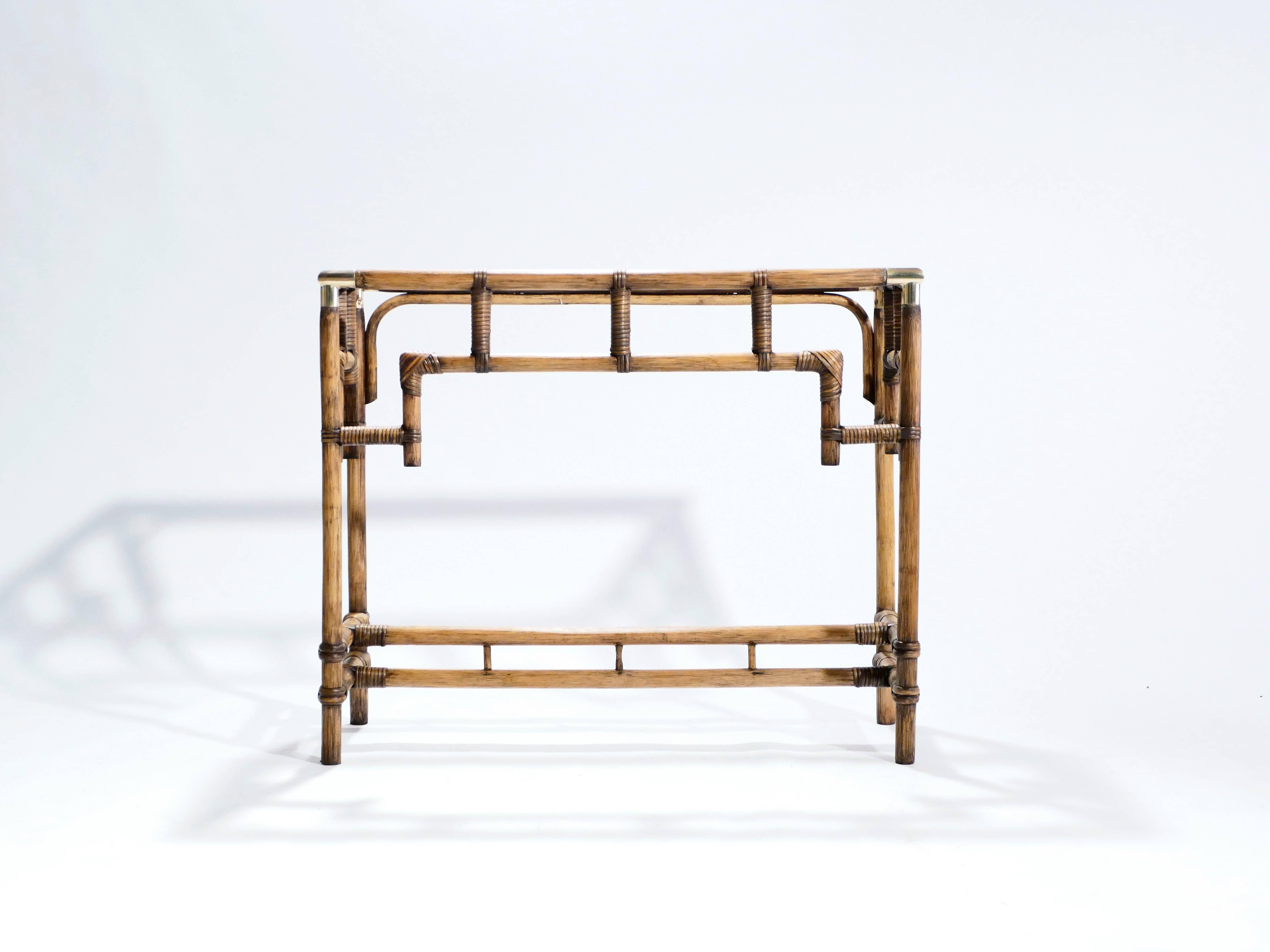 For a decorative entranceway piece, this console table is made largely from beautiful natural bamboo, with luxe displays of brass on the joints. Its surface is transparent glass. The piece was designed in the opulent Hollywood Regency style, most