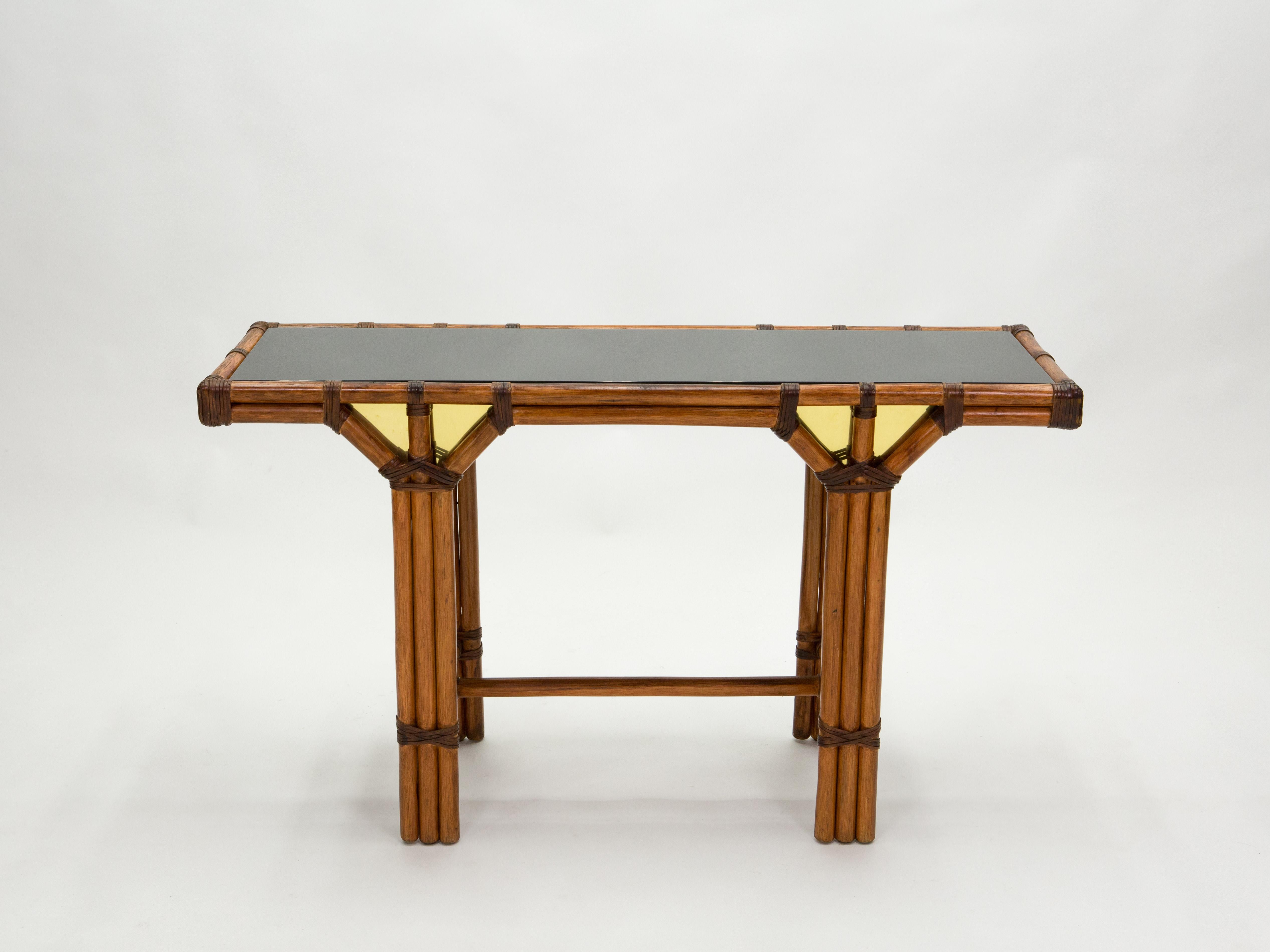 This beautiful console table was made from natural bamboo, with leather joints and luxe displays of brass inserts on the front and back, in the early 1970s in France. It features a slick black Opaline glass top. The piece was designed from the