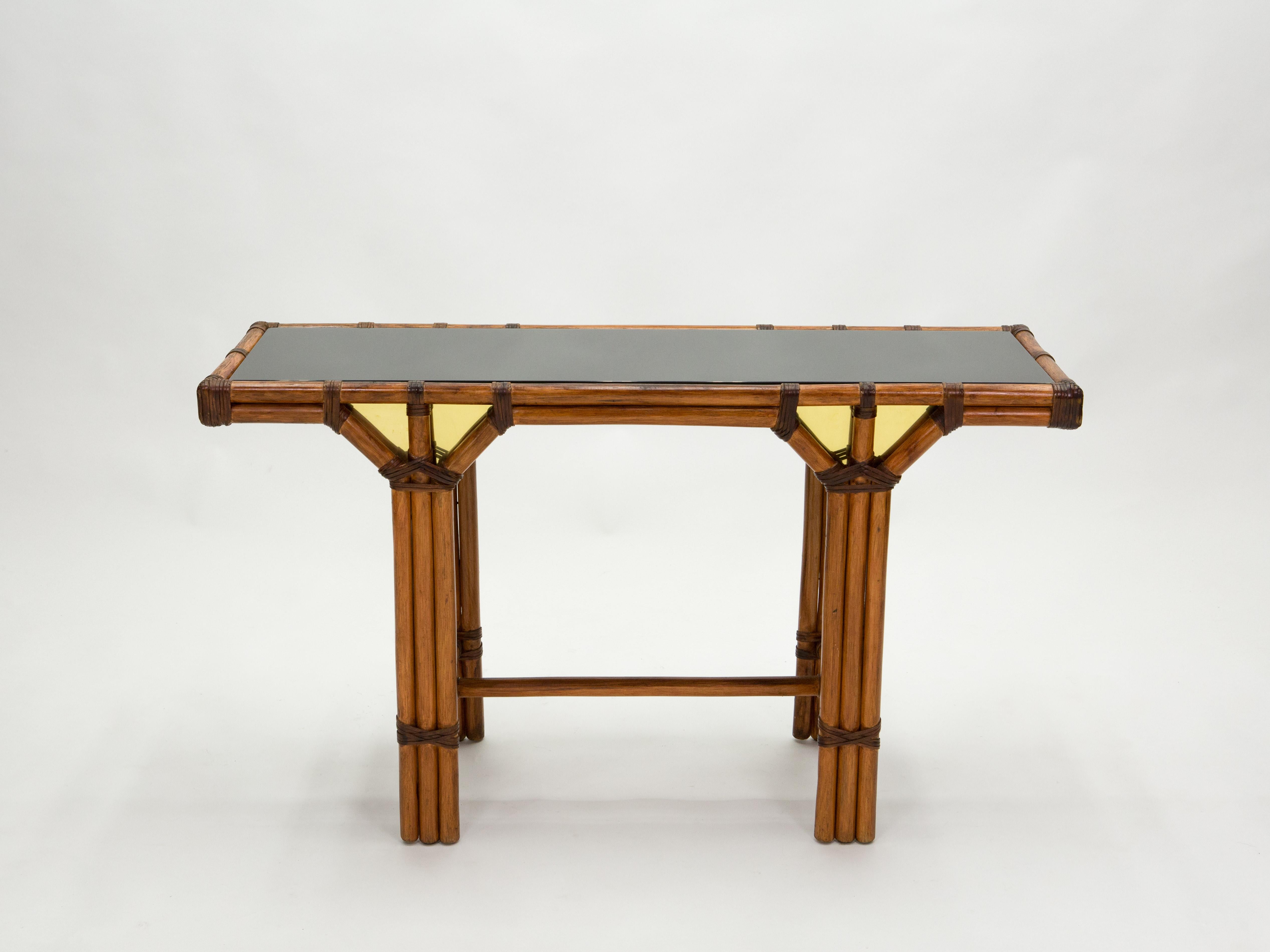 Cette magnifique table console a été fabriquée en bambou naturel, avec des joints en cuir et de luxueux inserts en laiton sur le devant et le dos, au début des années 1970 en France. Il est doté d'un plateau en verre opalin noir. Cette pièce a été