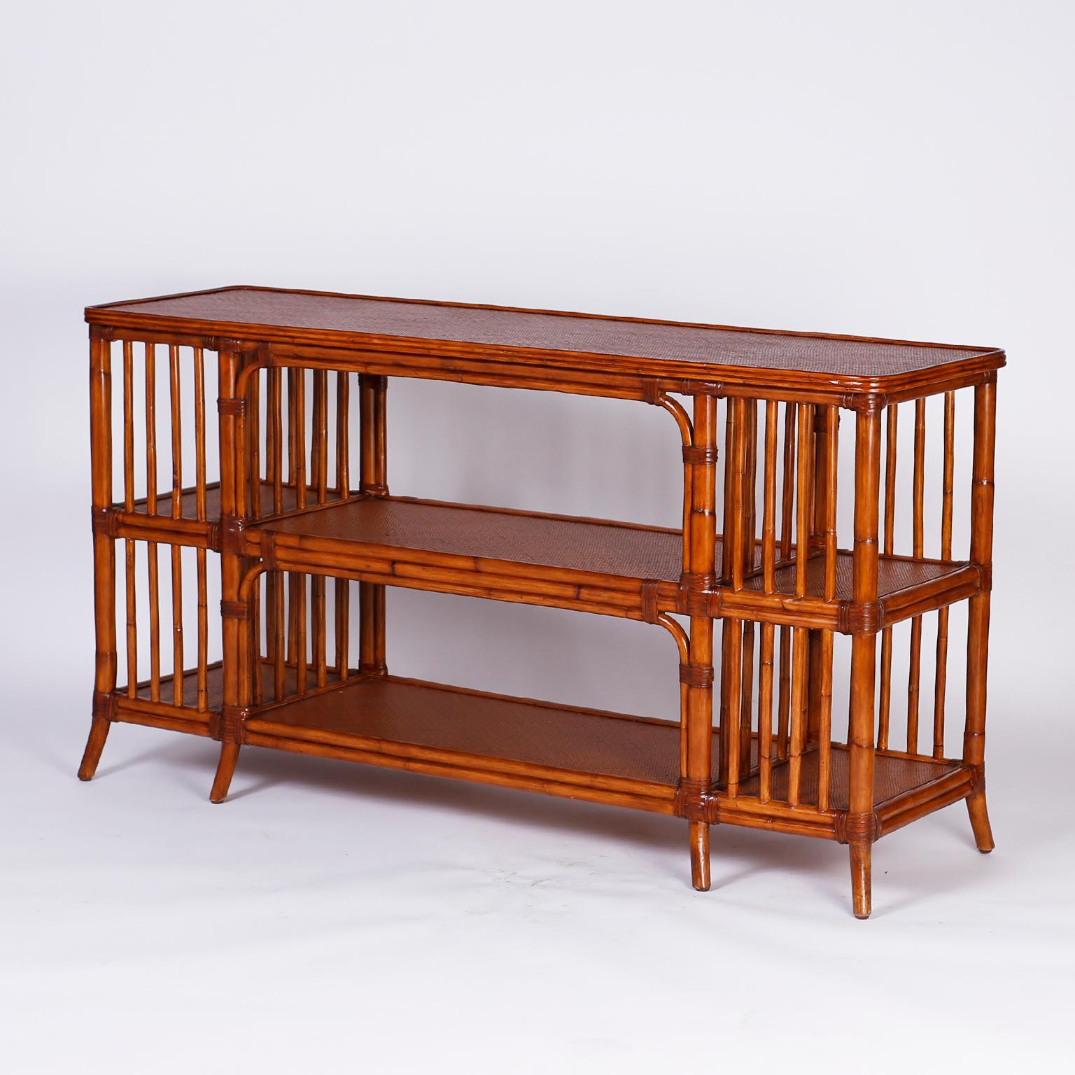 Midcentury three tiered console or server finished all around with a casual elegance featuring a bamboo frame wrapped with wicker reed at the joints, grass cloth surfaces on all three tiers, and stylish splayed legs.