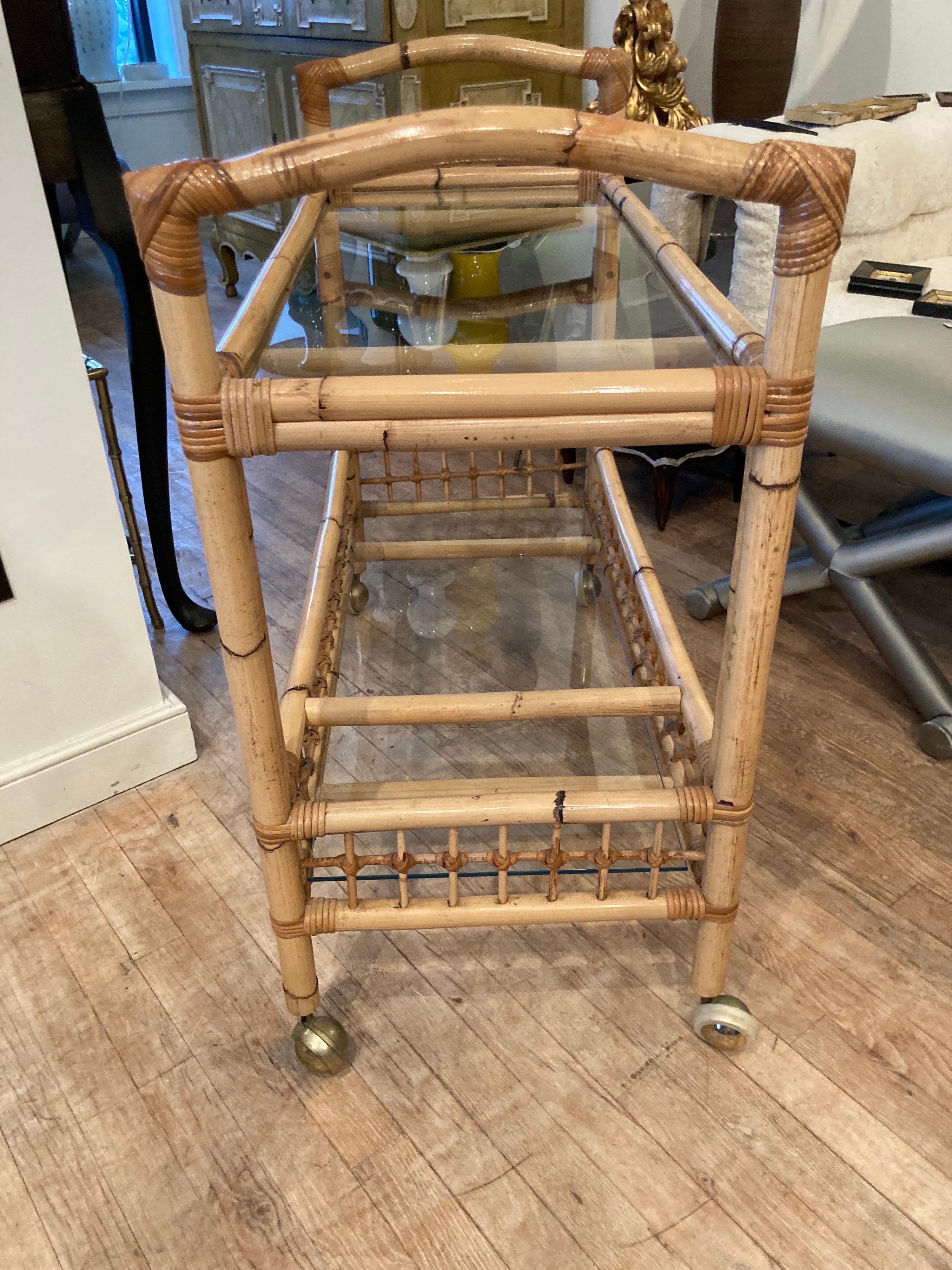 Bamboo and rattan bar cart on brass castors with glass shelves.
