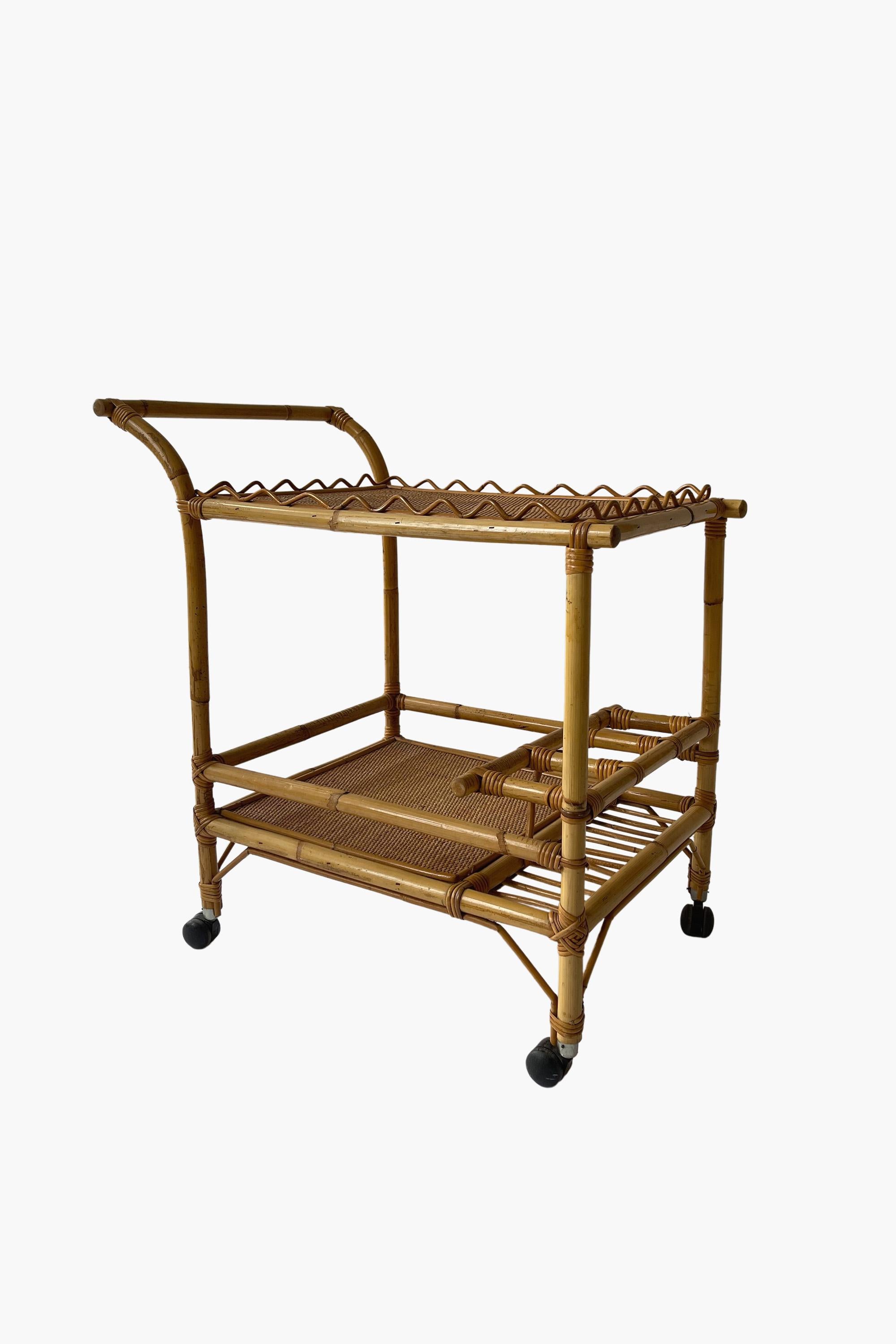 Bamboo and Rattan Bar Trolley with Scalloped Detail, 1960s

The bottom tier comprises a shelf in woven rattan and three bottle compartments. The top is covered in rattan matting with a scalloped gallery made in steam bent cane. 

Castors could be