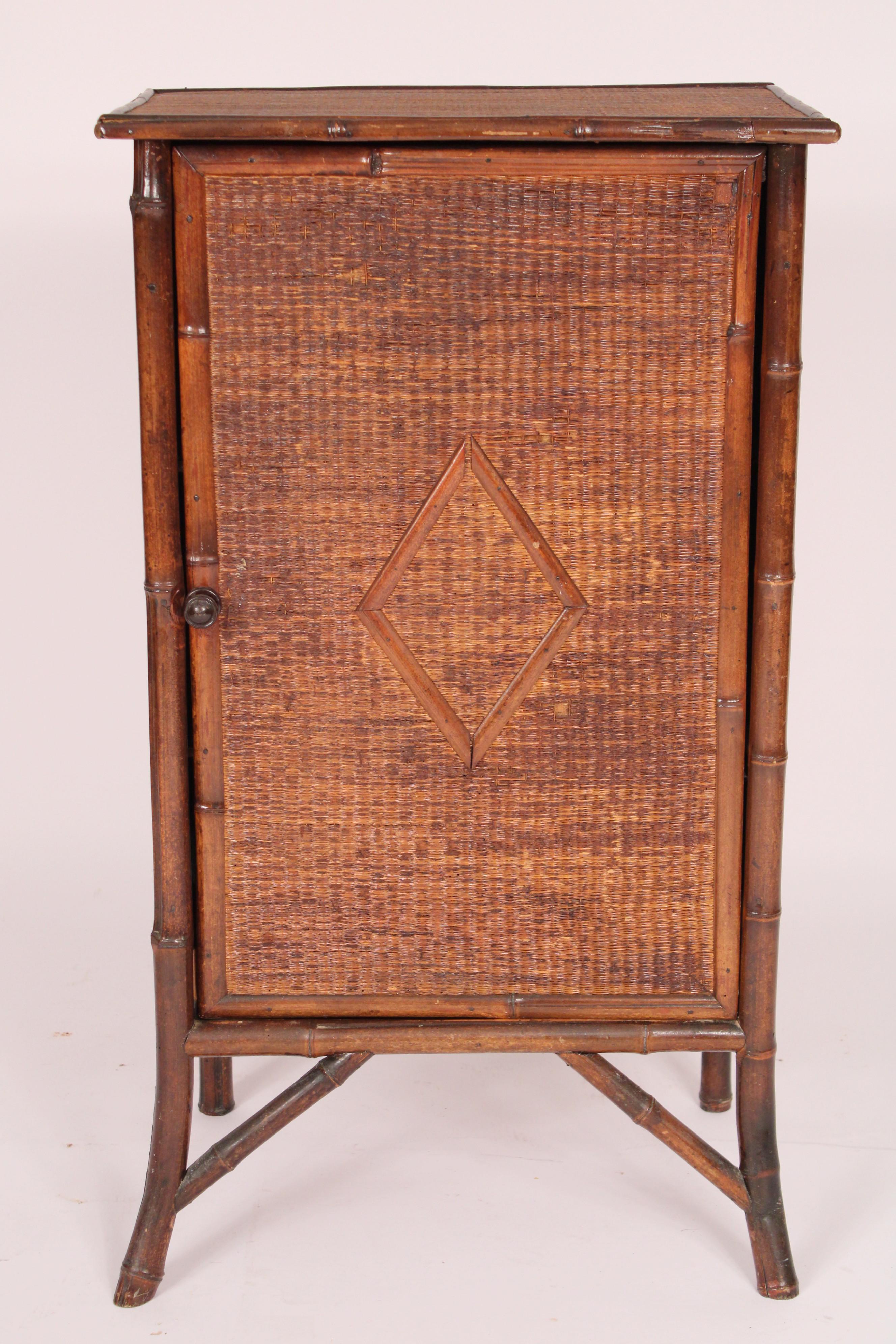 Bamboo and rattan single door cabinet, circa 1930s. With an overhanging rattan top with bamboo borders, single door with central diamond design, interior with 3 shelves, splayed legs with bracing.