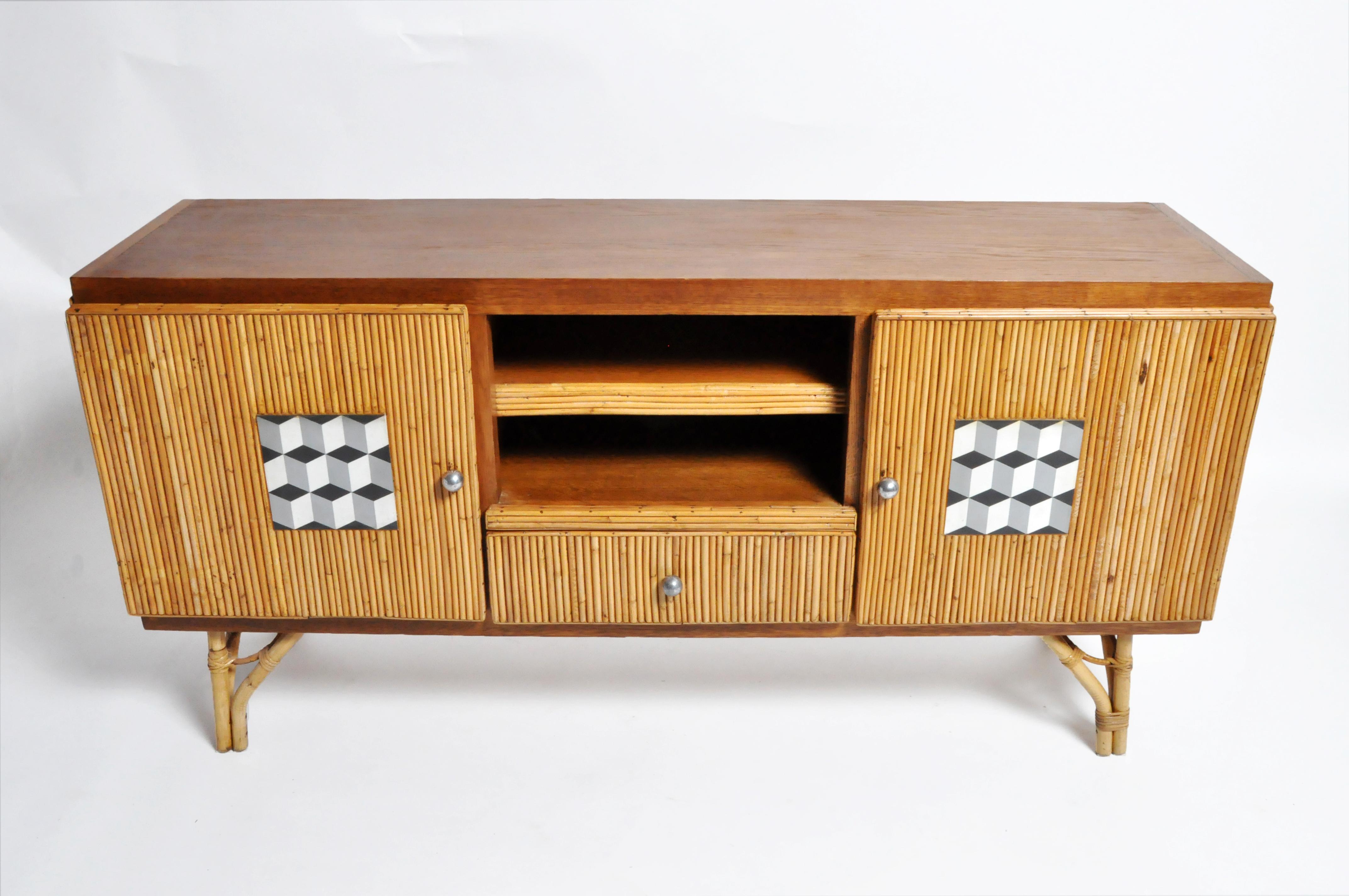 This tropical style “Tiki” sideboard has bamboo legs, a wood frame, a wood top and a decorative geometric-patterned insert on each door. This piece is from France and was made from bamboo and rattan, circa 1960. Knobs, made from brushed steel, are