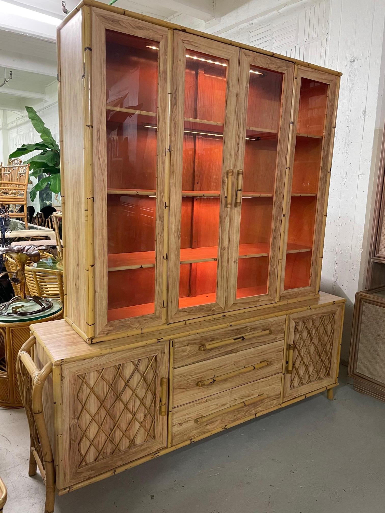Large vintage display cabinet features a unique sculptural rattan frame and reeded fretwork on doors and sides. Faux wood veneers and lighted display shelves. Good condition with minor imperfections consistent with age.