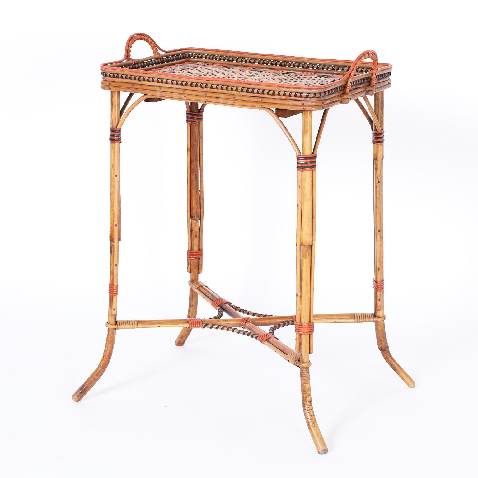 Serving stand or bar featuring a rattan and painted rattan tray style top with a herringbone center bordered by geometric designs and wrapped handled. The bamboo base has reed highlights and splayed feet.