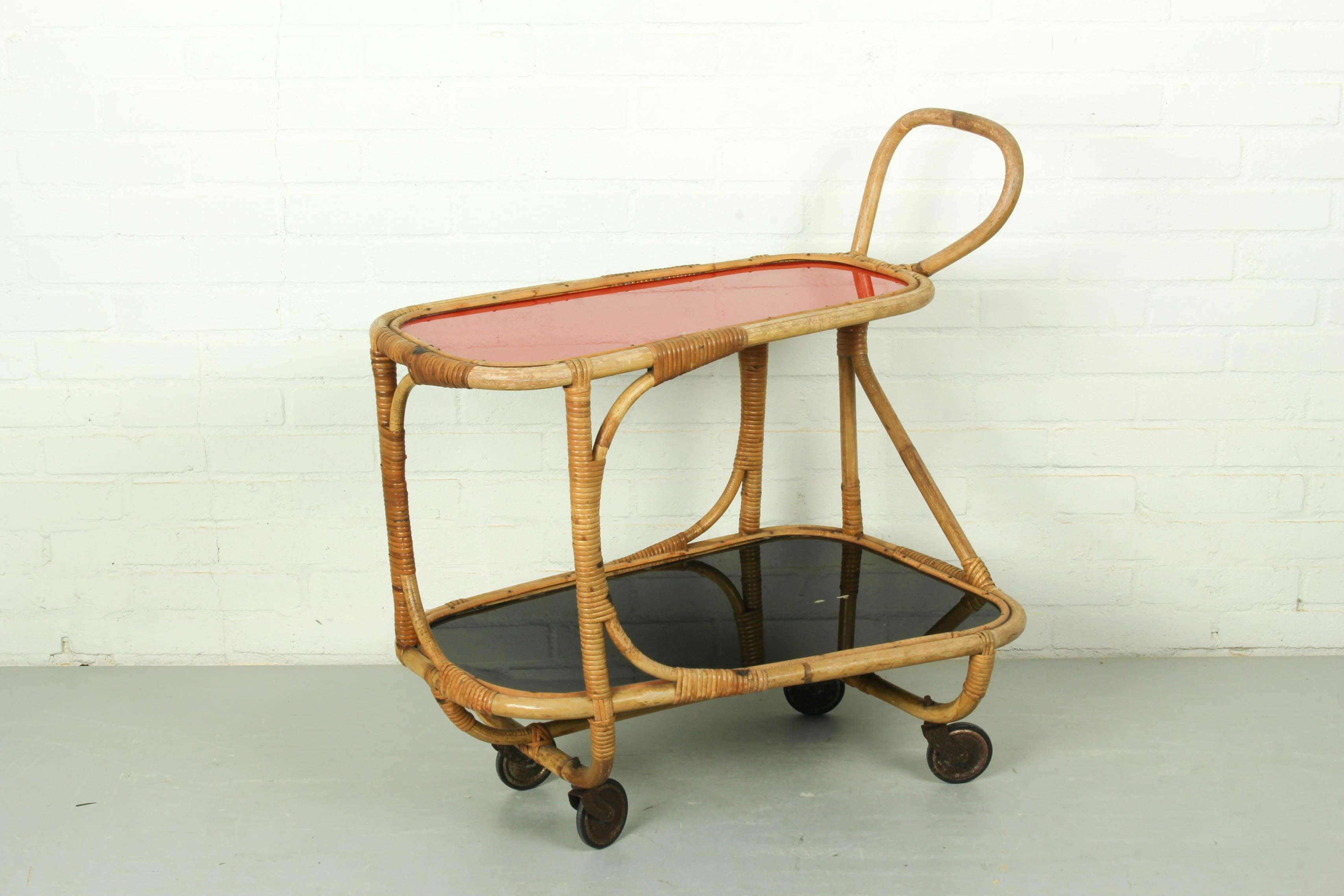 This bamboo / rattan bar cart from the 1940s features a red and a black shelf. Vintage, Mid-century, Hand-crafted. Dimensions: 76cm H, 73cm L x 45cm D.
  