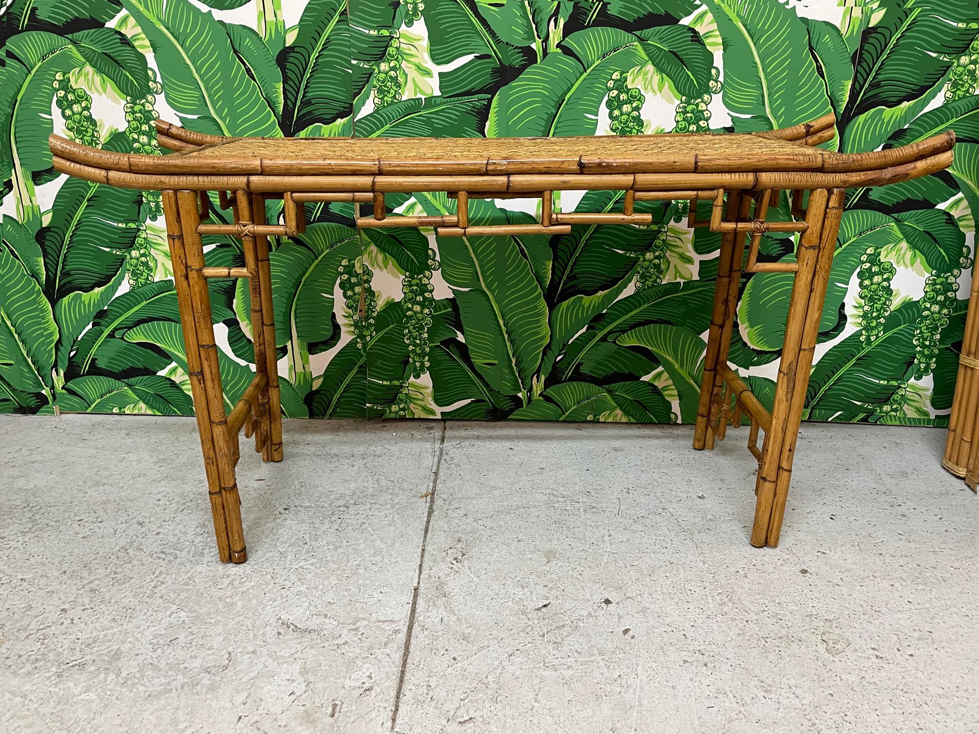 Vintage bamboo console or altar table features Asian chinoiserie styling with everted ends and decorative bamboo apron and spandrels. Top is veneered in woven wicker. Good condition with imperfections consistent with age, see photos for condition