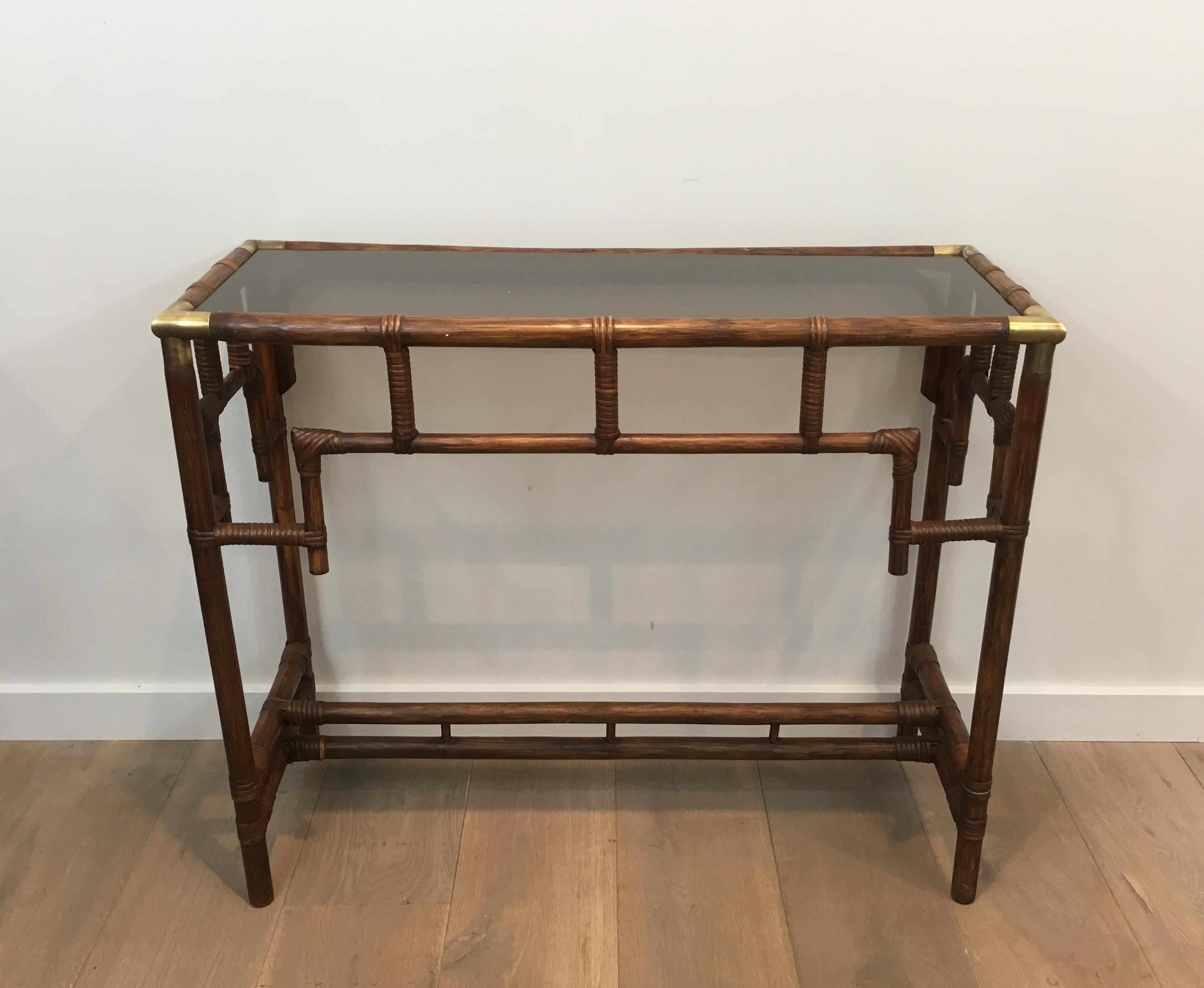 This unusual console table is made of bamboo with brass corners and smoked glass shelf. This is a French work, circa 1970.