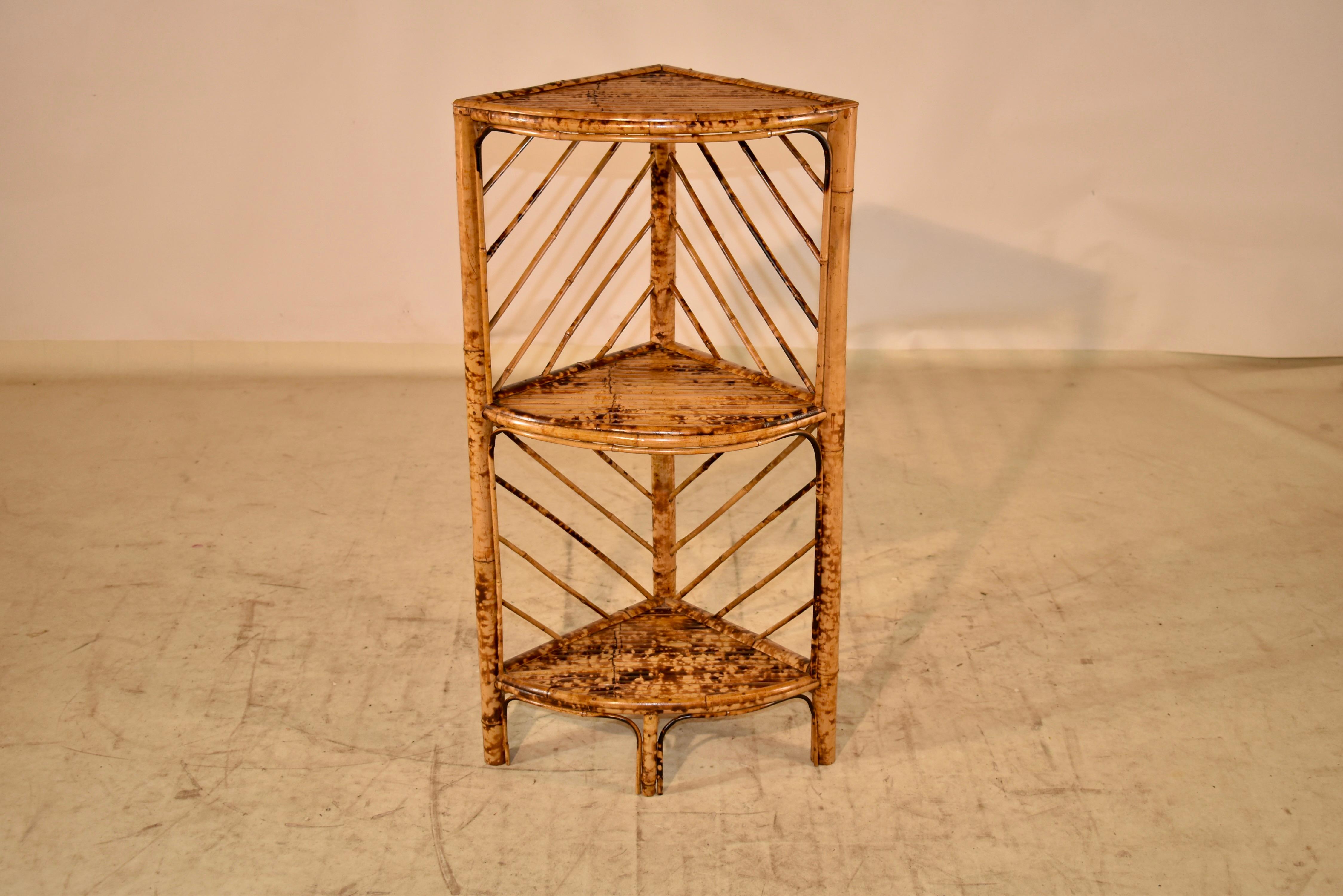 Mid-Century bamboo corner shelf from England.  The piece has three shelves, counting the top shelf and sits nicely in a corner for a decorative accent.  the shelves are made from split bamboo pieces for added texture and the back of the shelf has