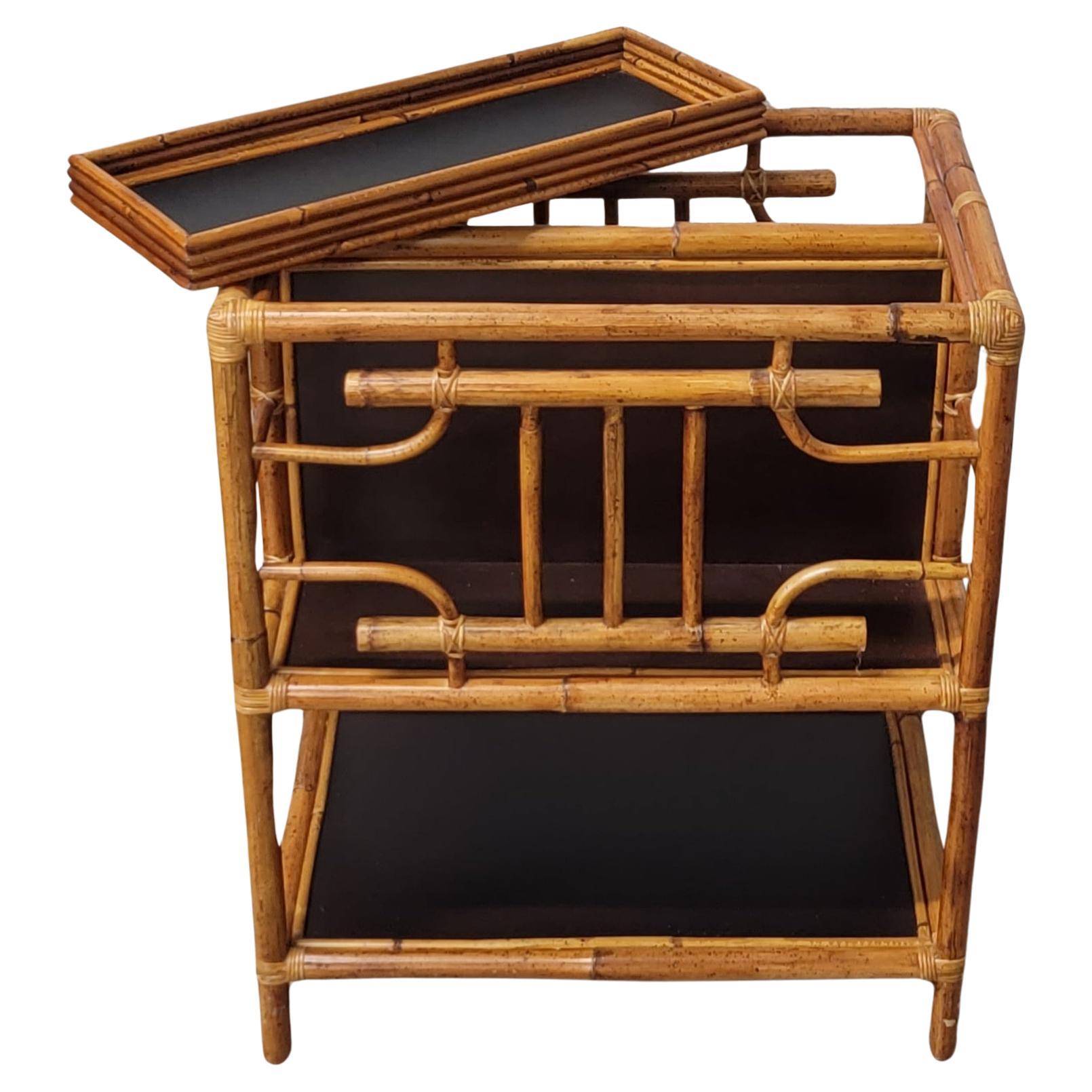 Vintage two-tier rattan stationary bar cart with removable pencil reed serving tray and fretwork. The Hollywood Regency style cart features an ebonized raffia divider and lower shelf. A versatile piece that can also be used as a magazine rack or to