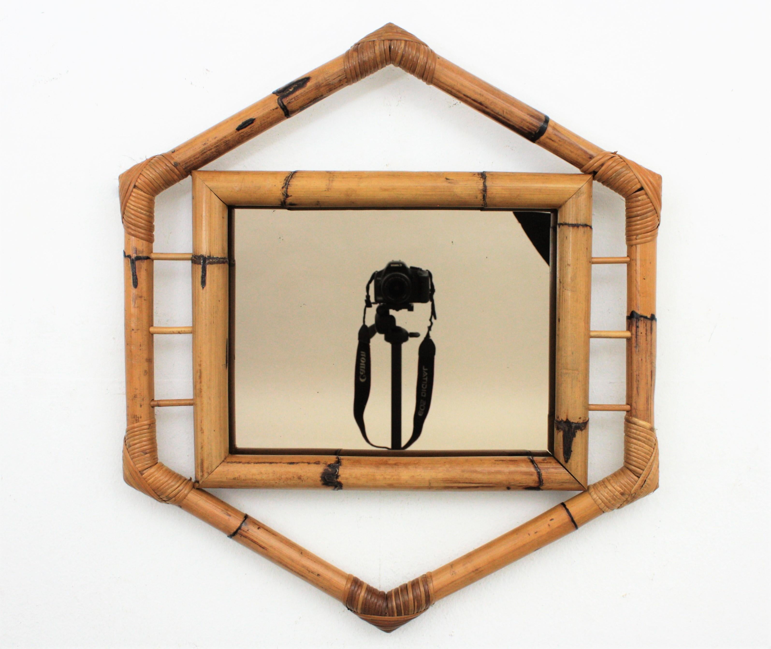 Ein wunderschöner sechseckiger Bambusspiegel mit kolonialen und orientalischen Tiki-Akzenten und geräuchertem Spiegel, Frankreich, 1950-1960.
Er ist aus dicken Bambusrohren handgefertigt, hat einige Rattan-Details und an den Ecken sind die