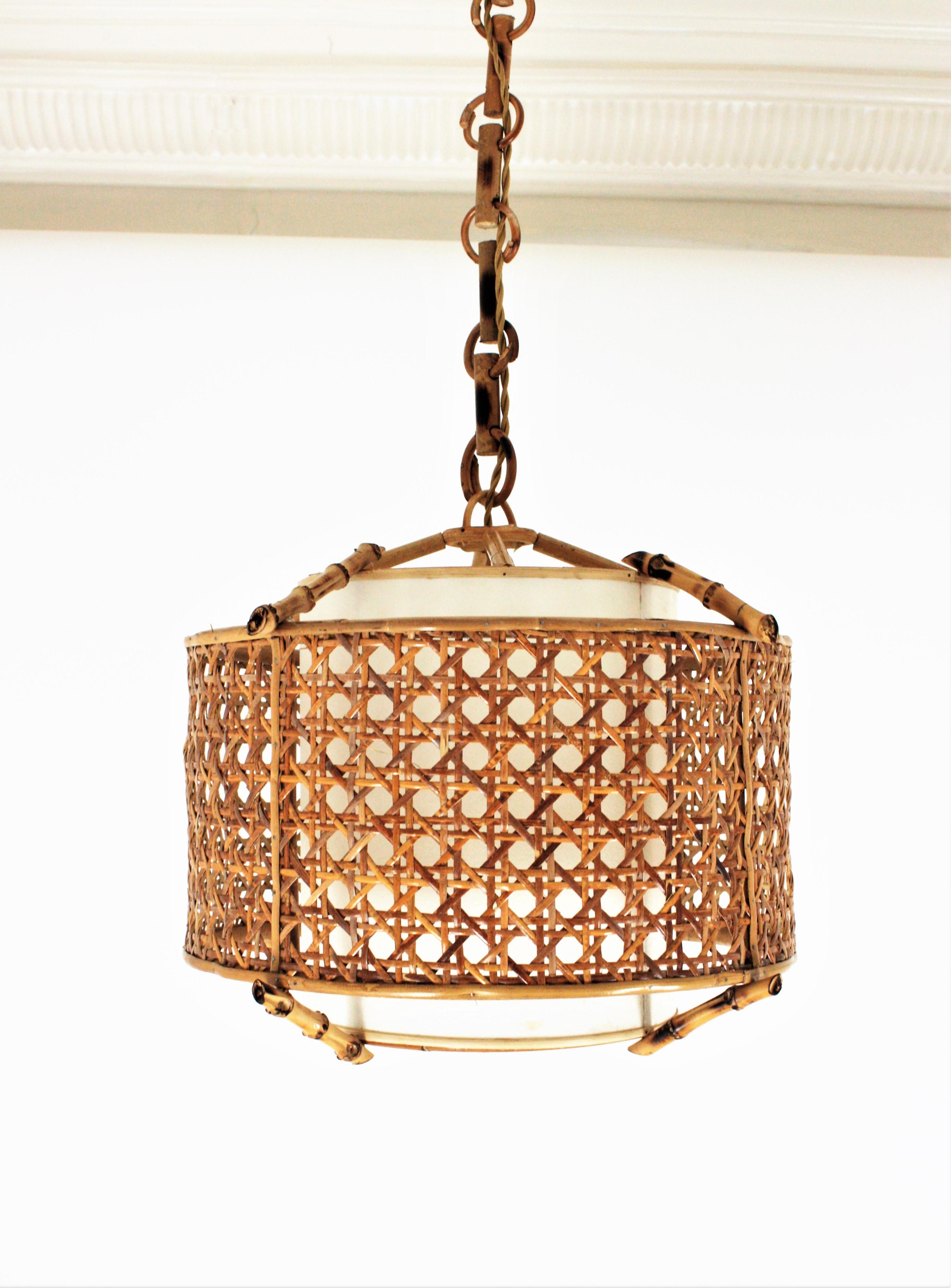 Spanish 1960s Mid-Century Modern bamboo and wicker wire large pendant lamp or lantern.
This suspension lamp features a drum shape woven wicker drum shaped lampshade accented by rattan and bamboo sticks. It has an interior cylindrical paper