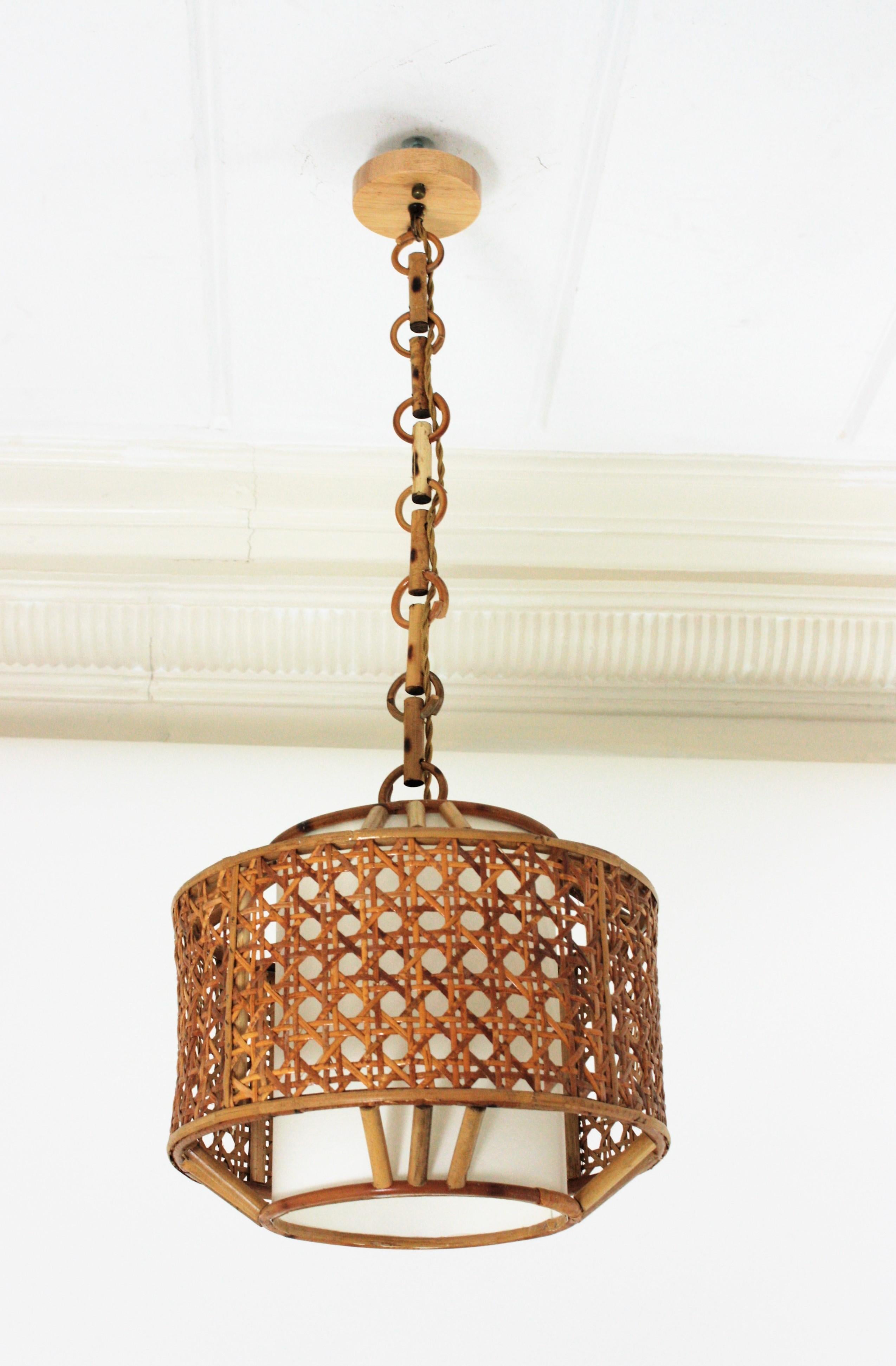 Spanish 1960s Mid-Century Modern bamboo and wicker wire pendant lamp or lantern.
This suspension lamp features a woven wicker drum shaped lampshade with triple bamboo sticks decorations. It has an interior cylindrical paper lampshade to diffuse the