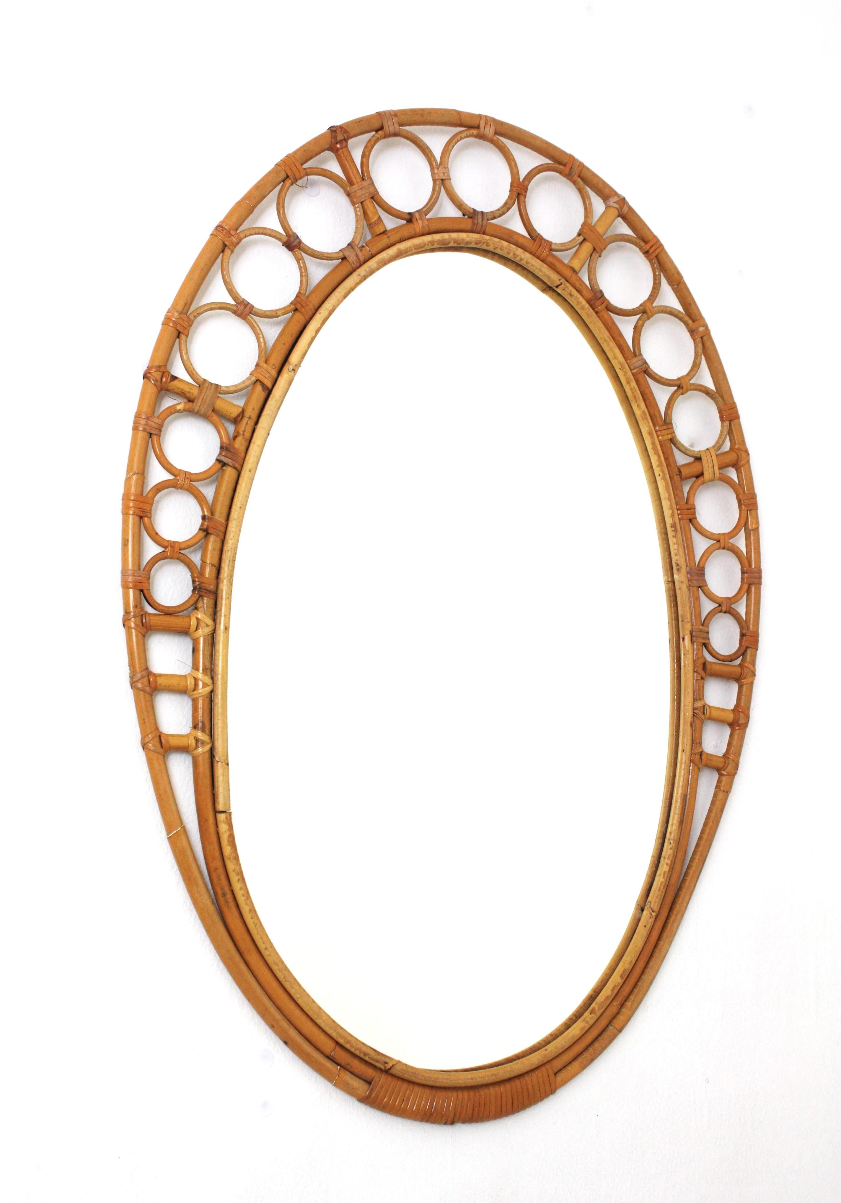 Large Oval Midcentury Rattan Bamboo Mirror. Spain, 1960s.
This wall mirror features an oval mirror glass framed by a bamboo / rattan frame with ring or circle details on the top and wicker / rattan tied accents.
Beautiful placed alone on a powder
