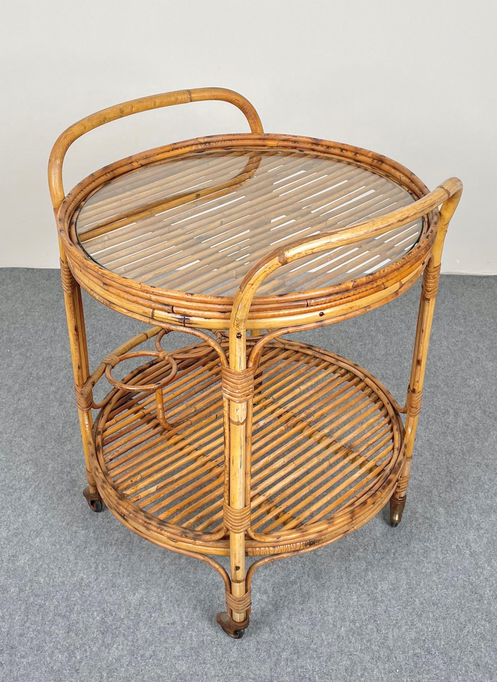 Round serving bar cart in bamboo & rattan structure featuring two shelves. The upper one is covered by a glass top and the lower one features three bottle holders. Made in Italy in the 1960s.