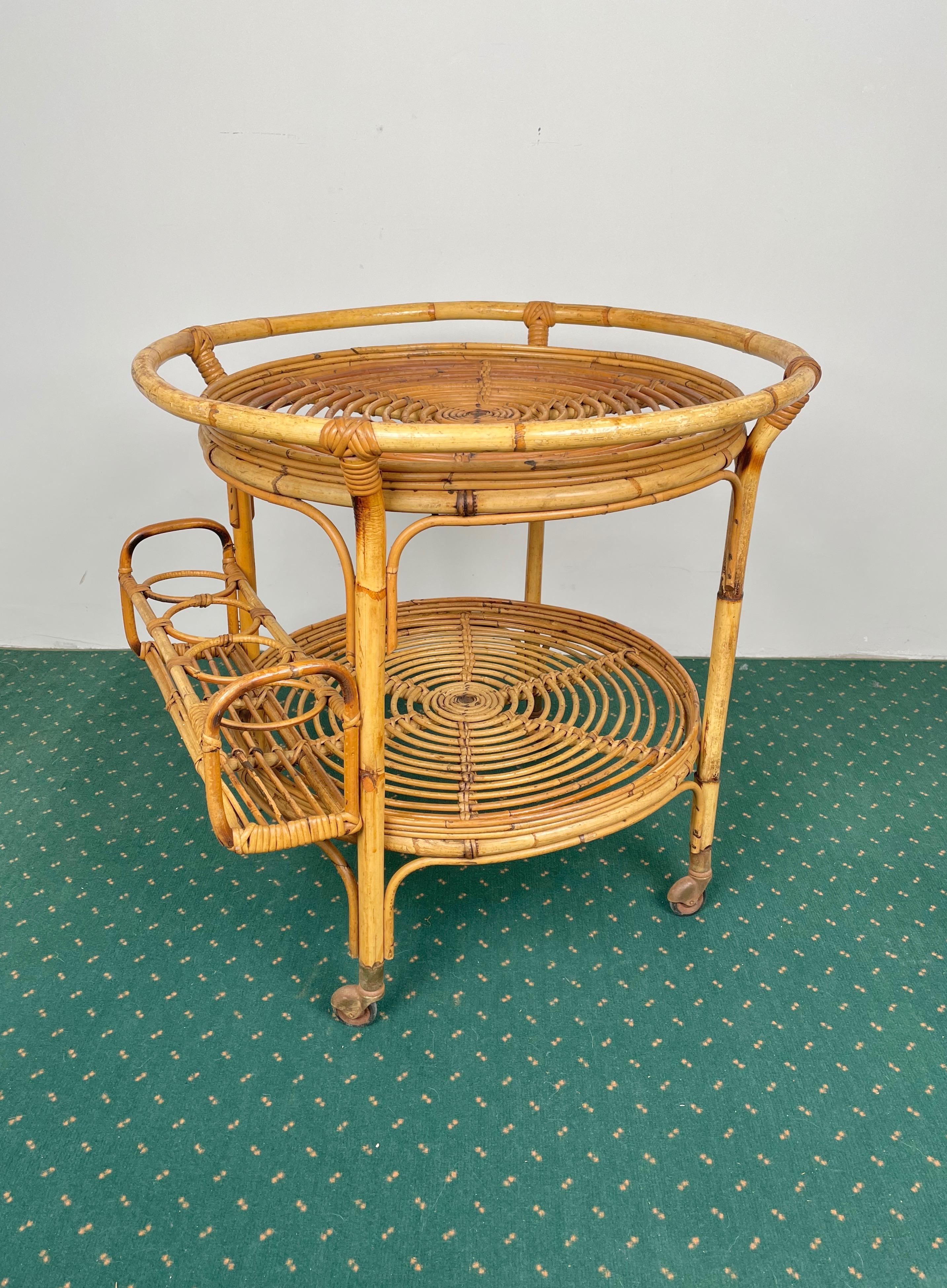 Elegant round serving bar cart in bamboo & rattan structure featuring two shelves. The upper one is framed by a bamboo handle and the lower one features four bottle holders mounted externally. Made in Italy in the 1960s.