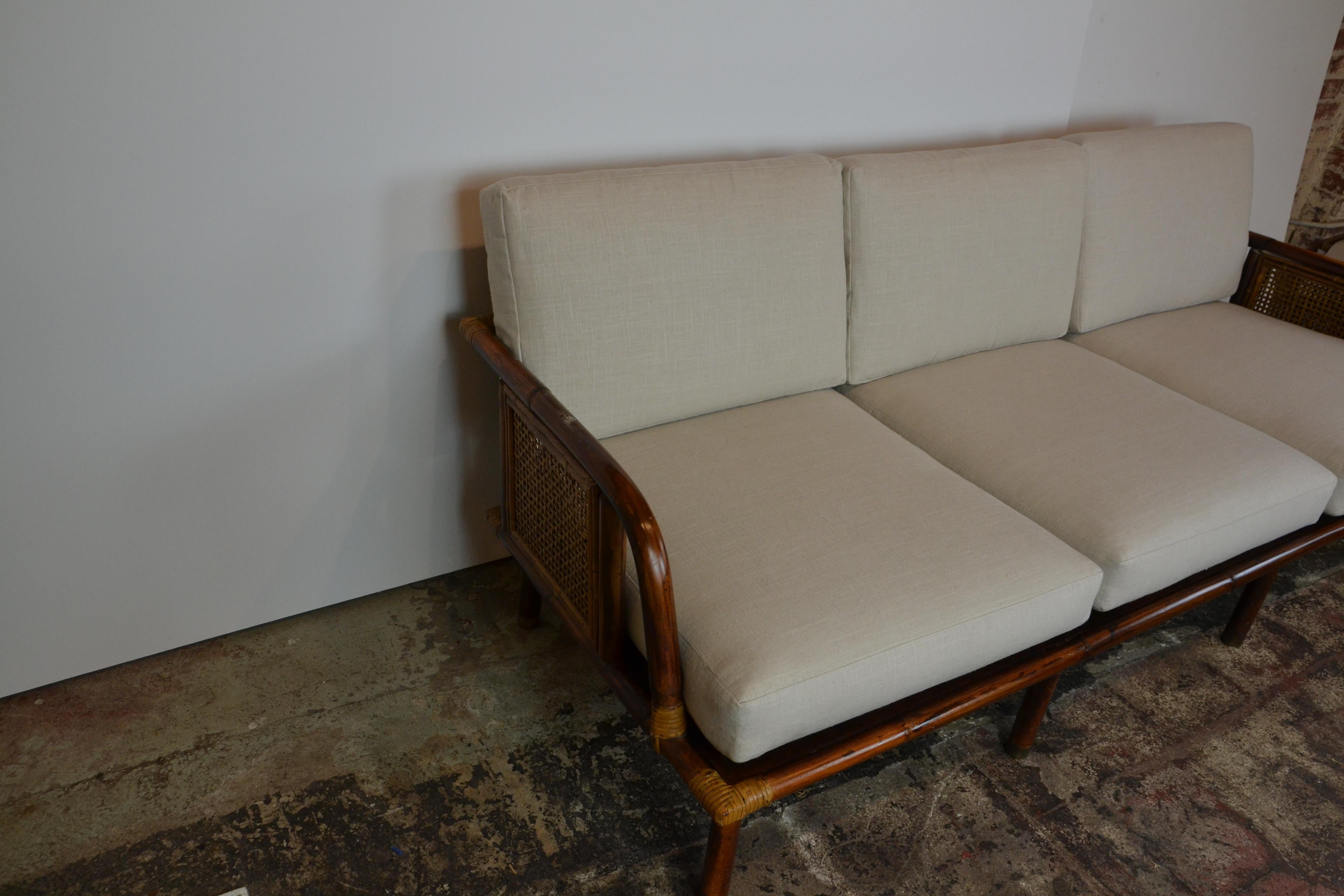 A beautiful 3-seat modern rattan and cane sofa from a limited series by Ficks Reed Company, circa 1950. Expertly crafted hardwood and rattan construction with cane panel detail. A fabulous design that is extremely comfortable. Newly upholstered in a