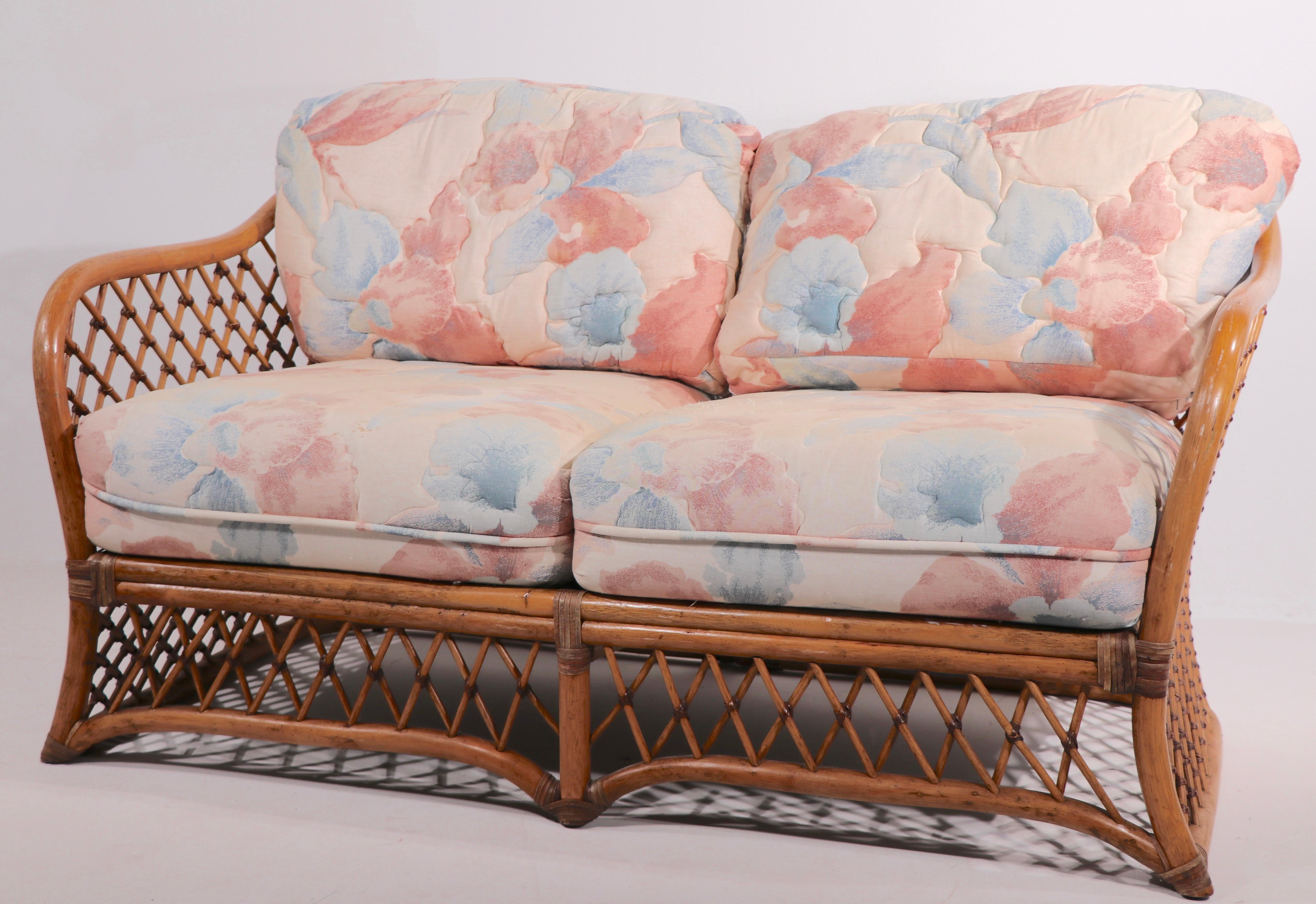 Chic bamboo settee, sofa, loveseat having a curved woven bamboo seat and back, on bamboo frame, with thick cushions. The sofa is in very good, original condition, showing only light fading to the fabric, normal and consistent with age. In the style