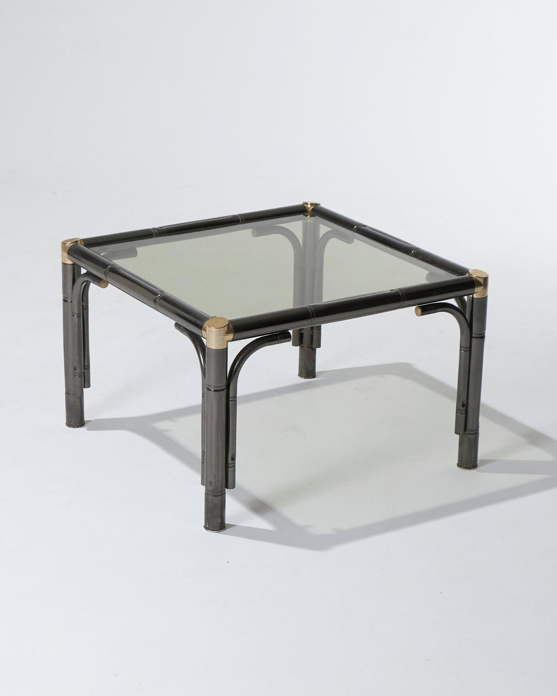 Mesa de centro de estilo Maison Jansen, fabricada hacia 1980. Estructura de metal patinado con diseño estilo bambú, que combina los acabados bronce de cañón y dorado. Cubierta con una superficie de cristal ahumado. En buen estado general.