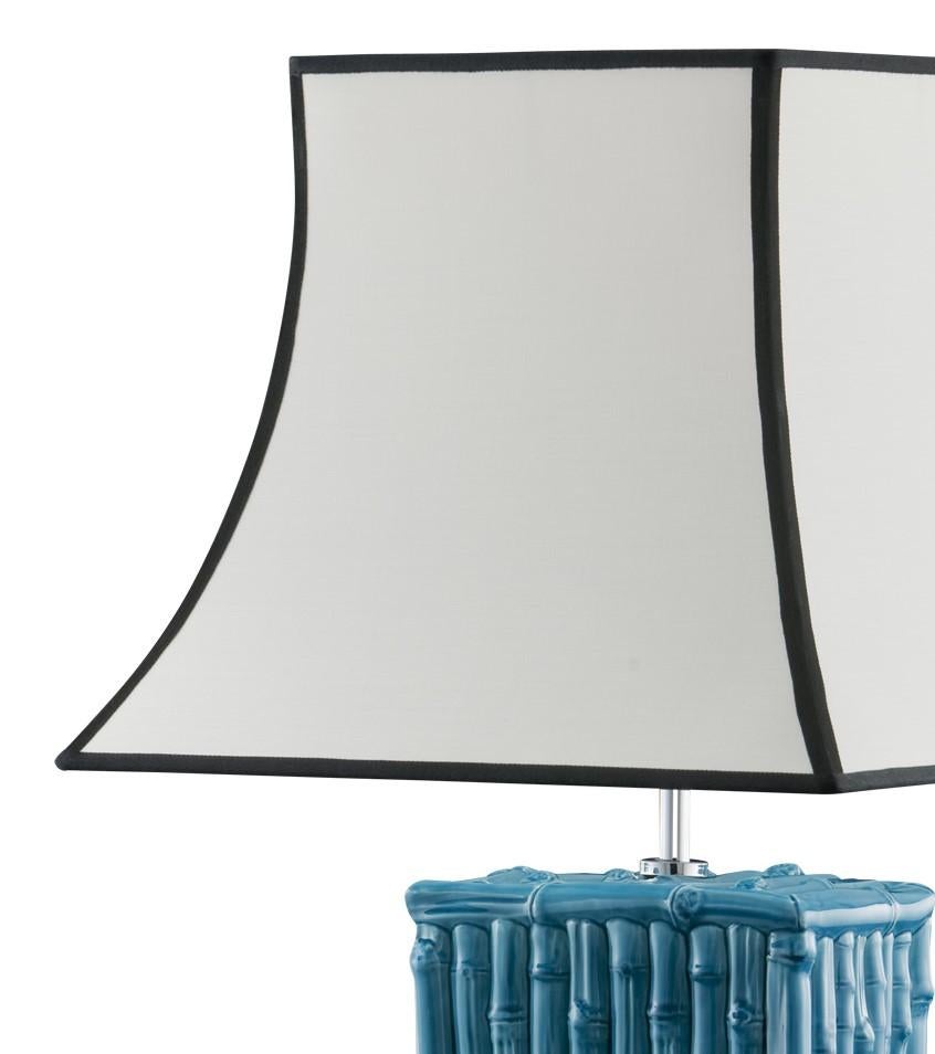 The ceramic stand of this striking lamp reproduces a structure made of bamboo sticks with a vivid turquoise color. The elegant white shade is accented with black giving the piece an elegant finish.