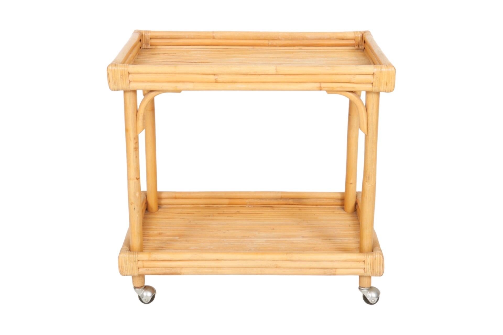 A bamboo and rattan bar cart with bentwood bamboo corners. Two tray like shelves are made with bamboo pieces with bamboo sides. Corners are secured with rattan binding and silver metal ball castors allow the bar cart to move easily in all directions.