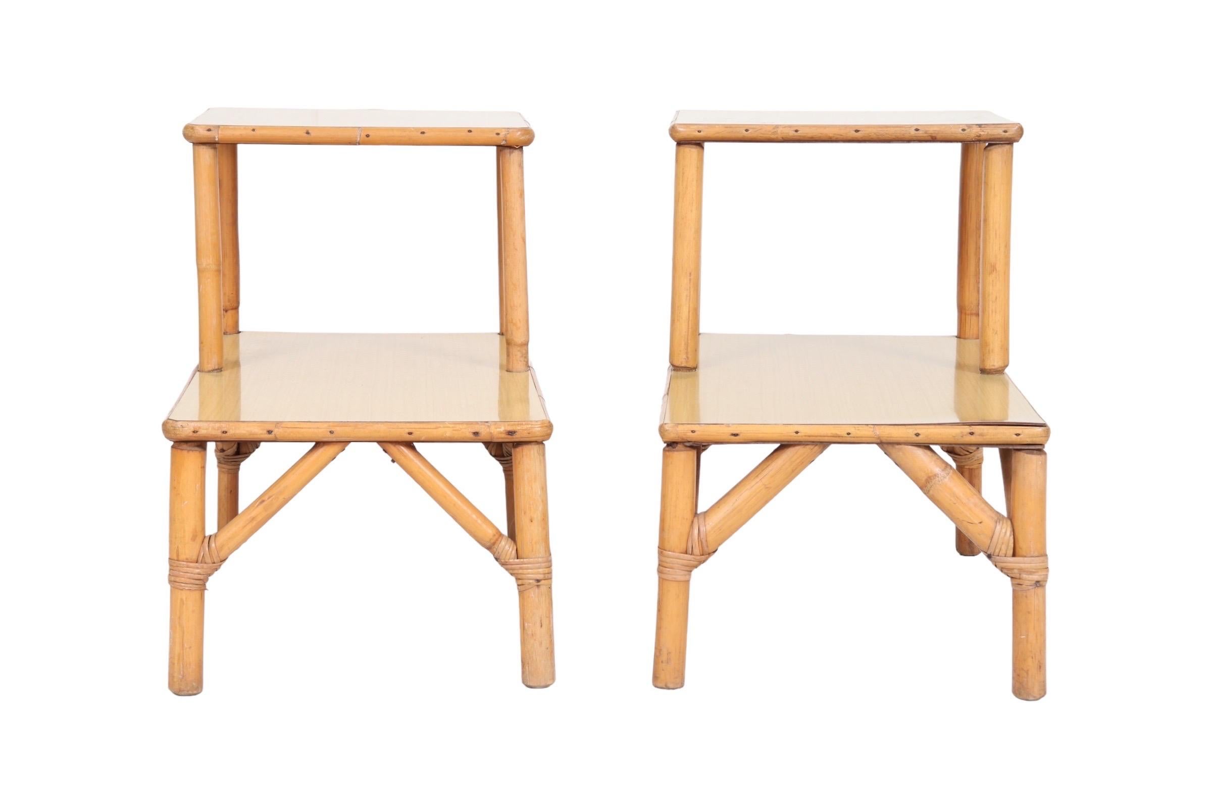 A pair of two-tier side tables made of bamboo. A squared top table over a rectangular lower table, both Formica, are supported on bamboo legs secured with rattan. Dimensions per table.
 