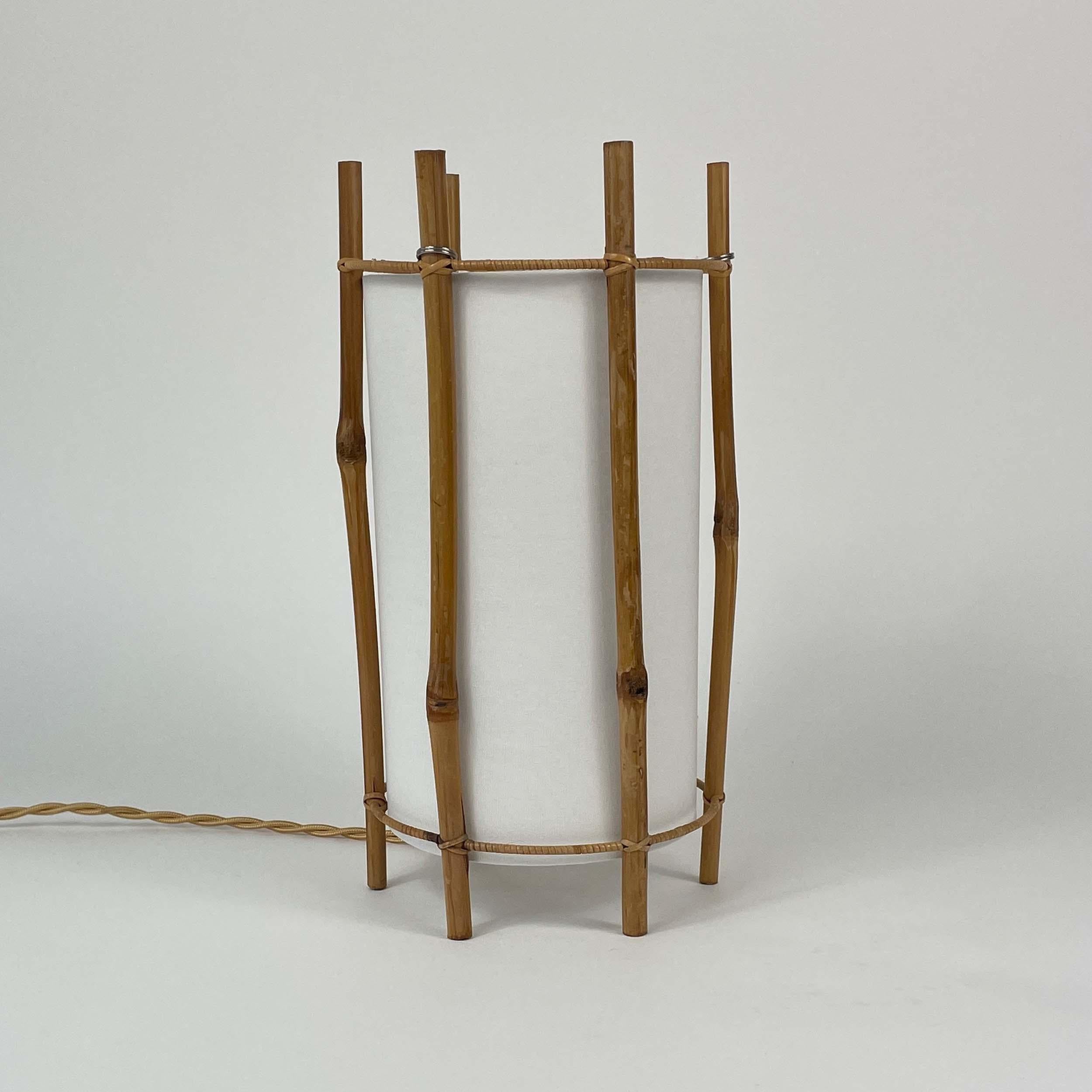 Esta insólita lámpara de sobremesa de diseño minimalista y natural fue creada por Louis Sognot y fabricada en Francia en la década de 1950. 

La lámpara está hecha de bambú con una pantalla cilíndrica de color blanquecino. El armazón está construido